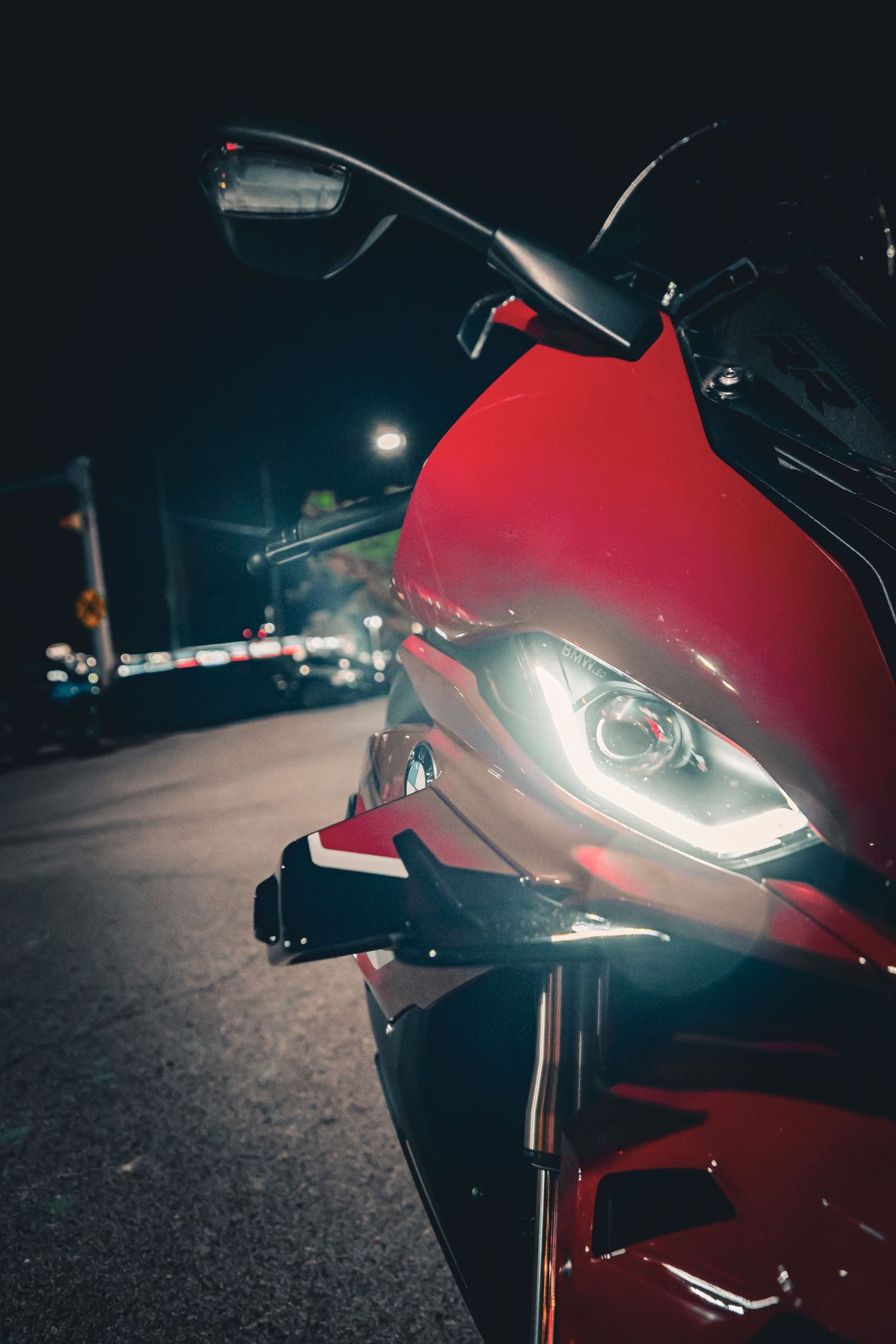 Close-up of a red sport motorcycle headlight glowing at night on a dark street.