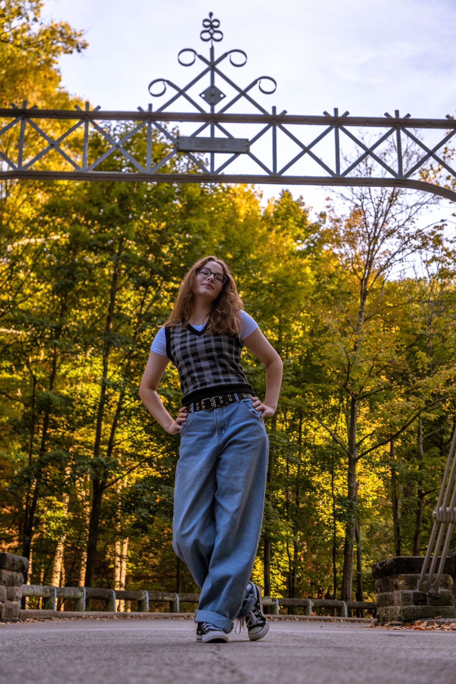 Person in casual wear poses playfully on an ornate metal railing during autumn season.