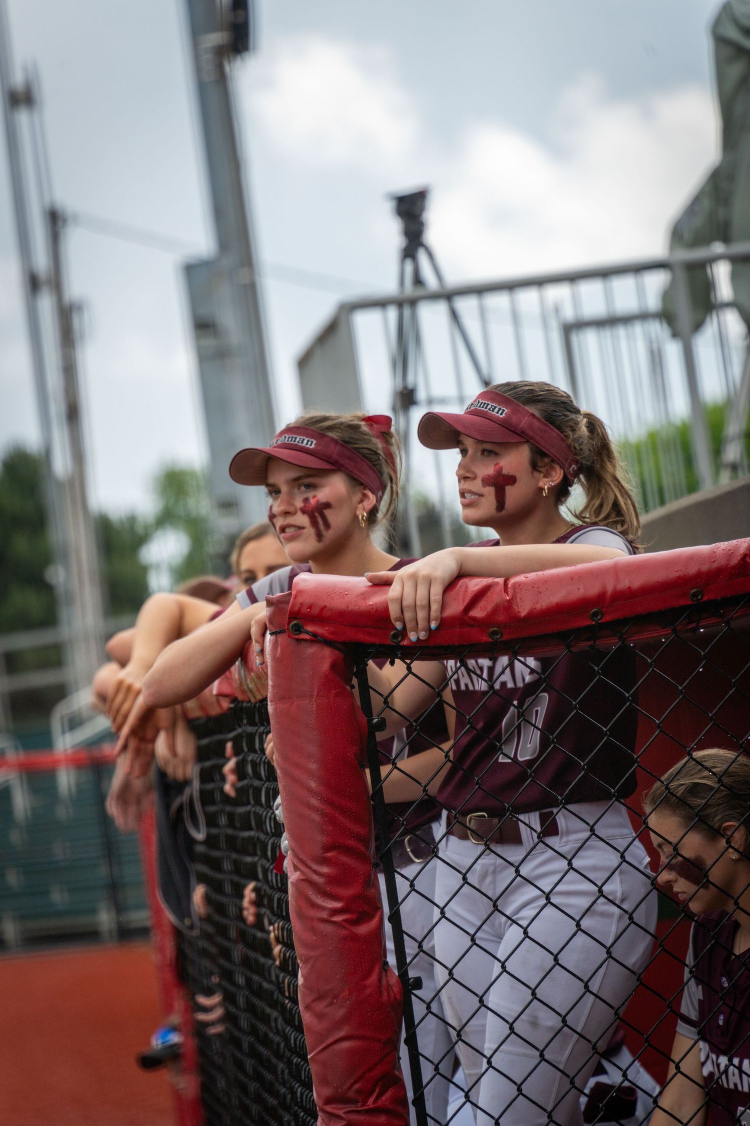 Team members leaning on dugout fence watching game action.
