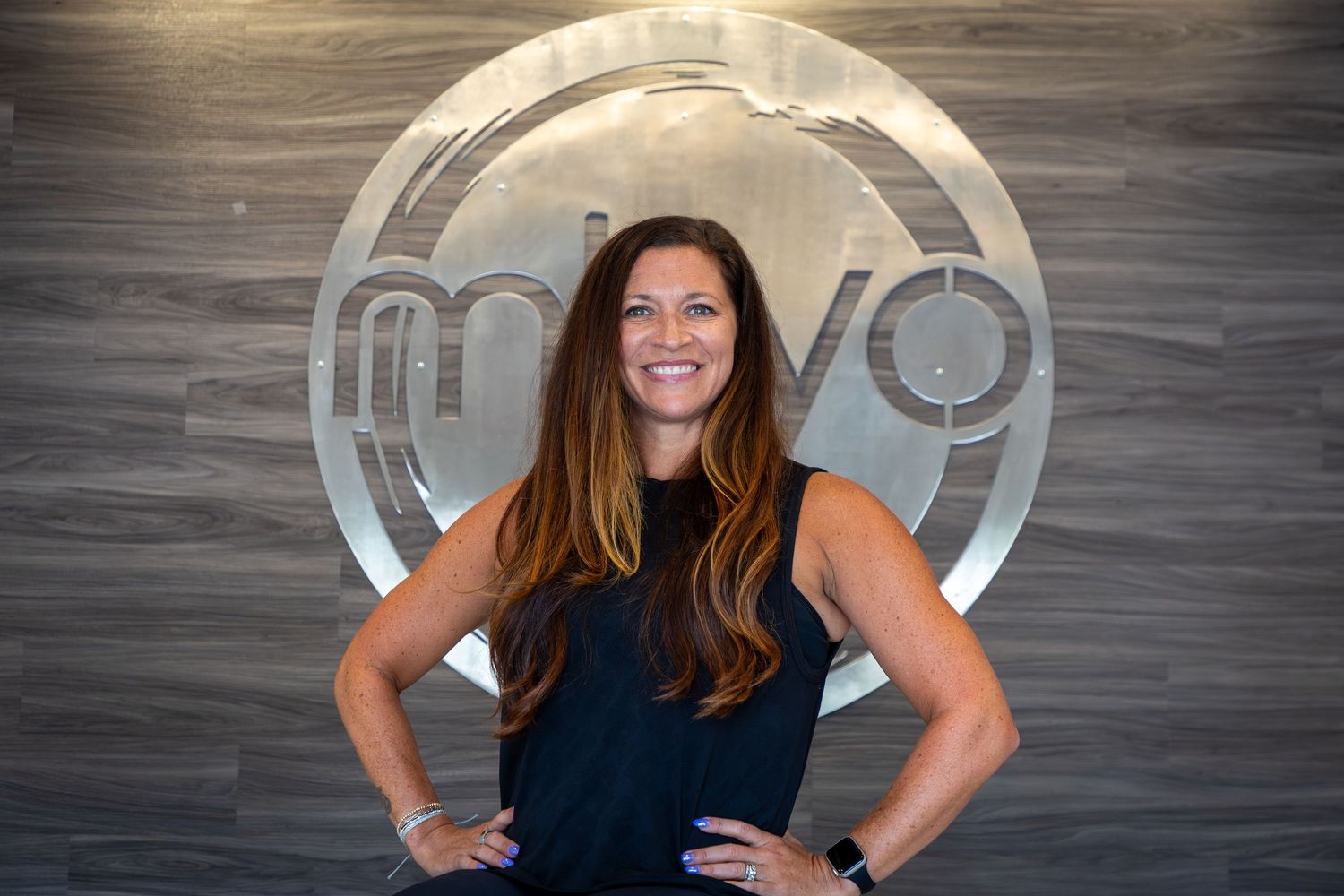 Fitness instructor striking confident pose against wooden wall with circular logo.