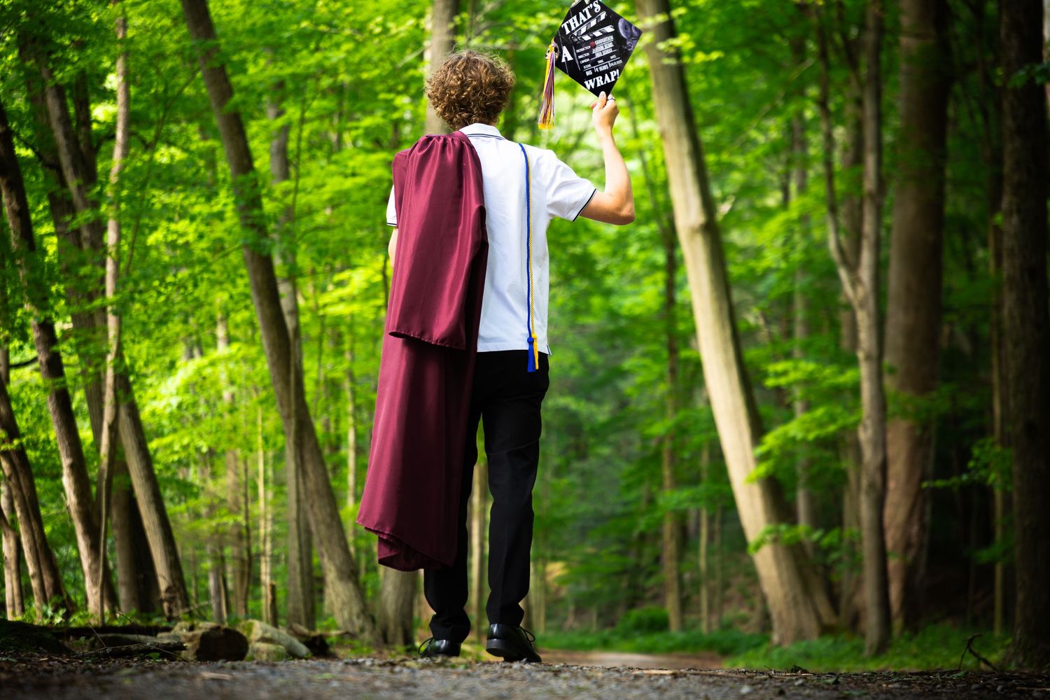 Forest path lined with trees creates natural backdrop for graduation photos.