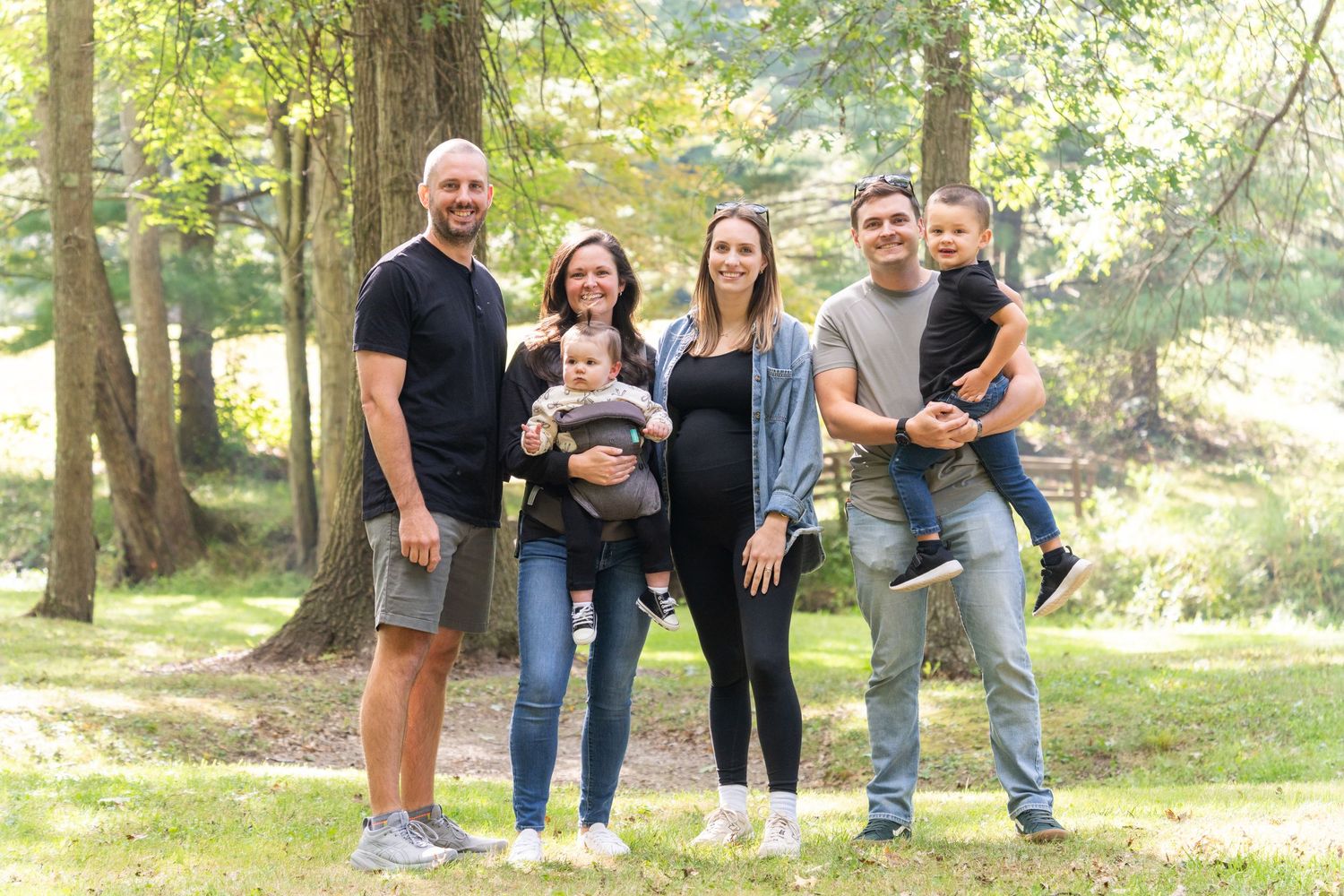 Group photo of family members posing together in a sunlit wooded area.