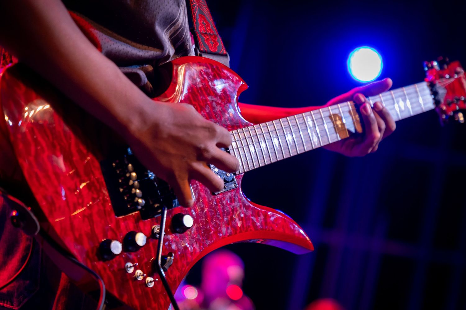 Musician playing a vibrant red electric guitar on stage under blue and purple stage lights.