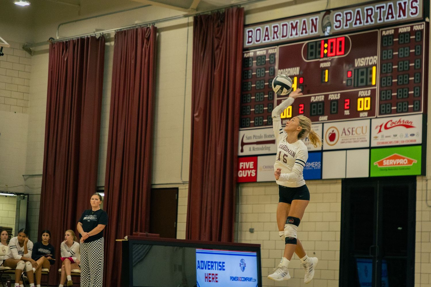 Scoreboard and spectators visible during indoor volleyball match.