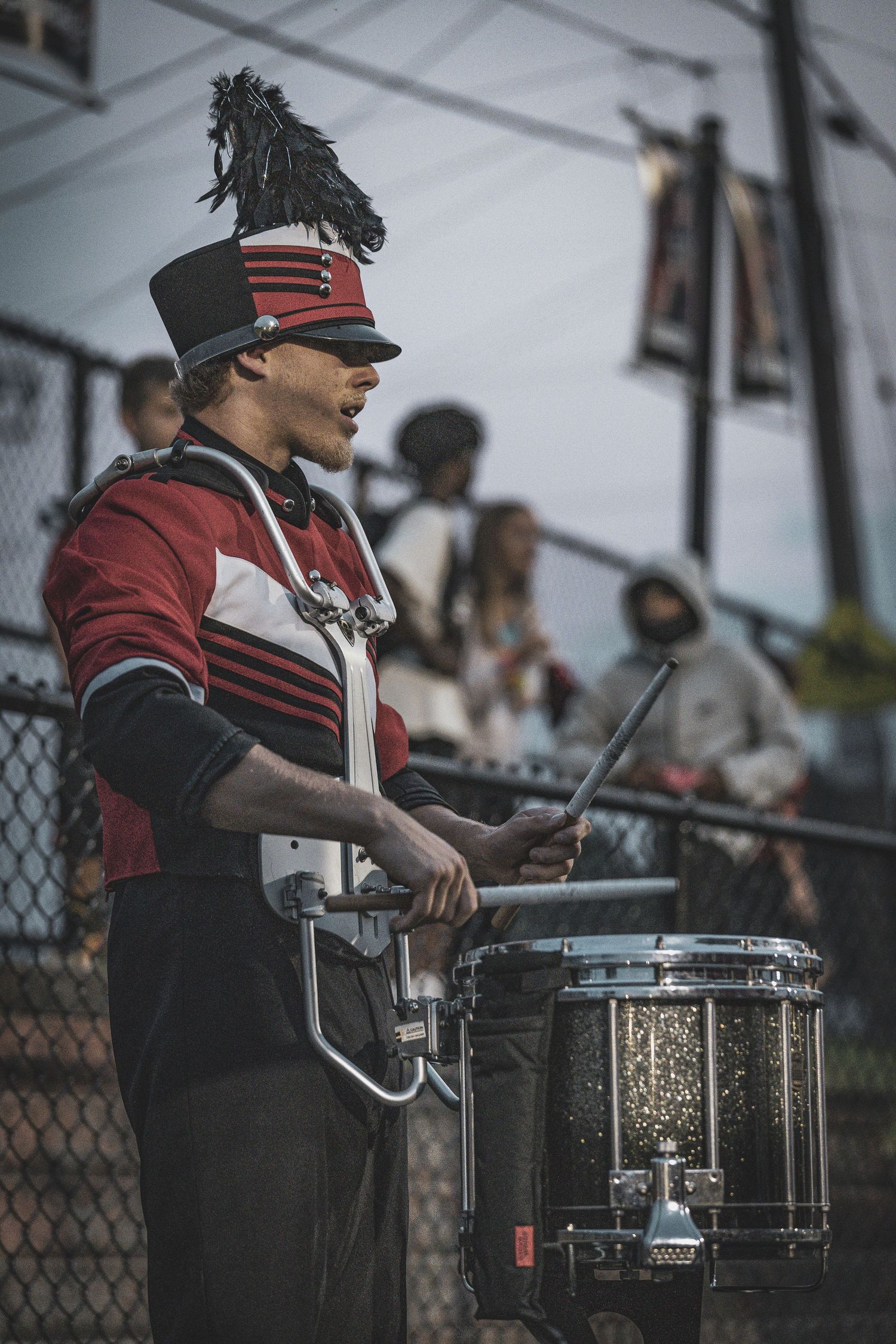 Drumline performers in black uniforms playing snare drums during a marching band performance.