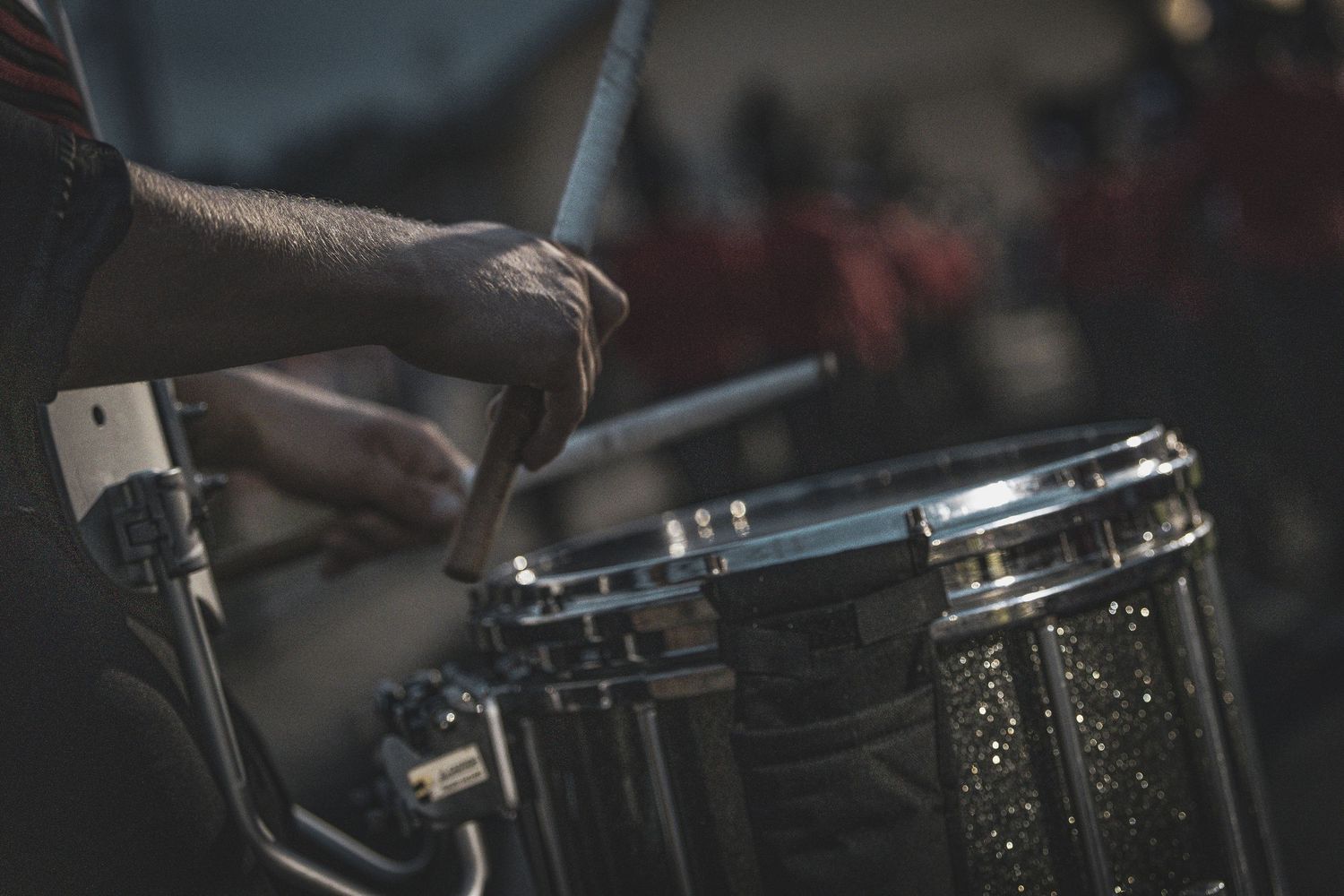 Close-up shot of hands playing a sparkly black snare drum with drumsticks.