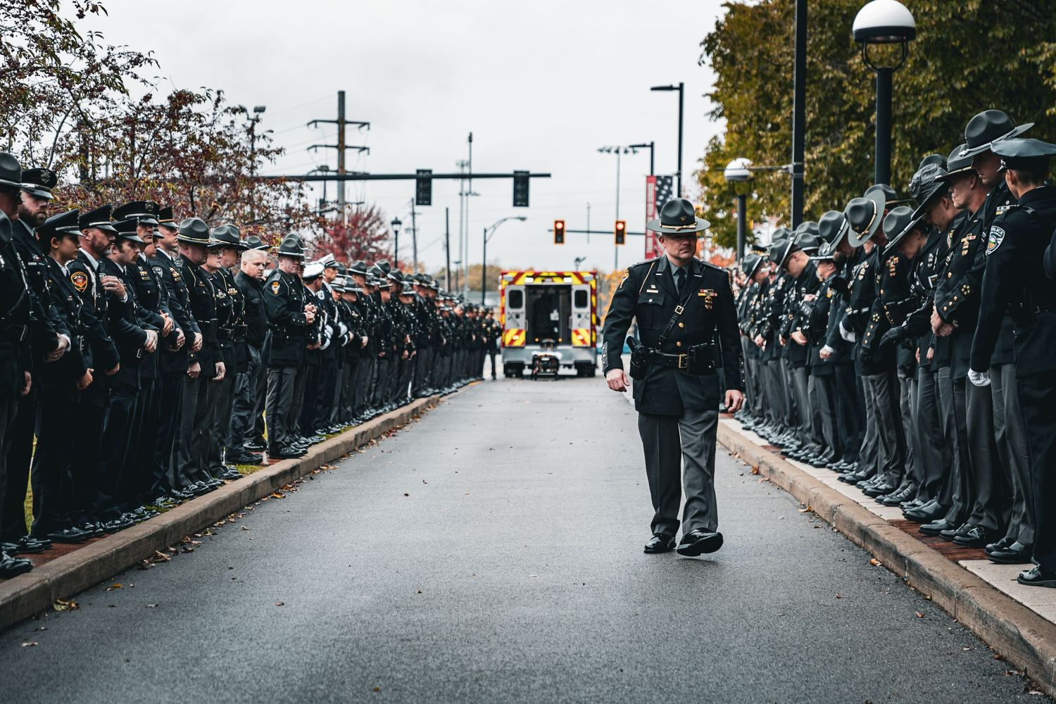 Officers form two lines along a street as a vehicle approaches in the distance.