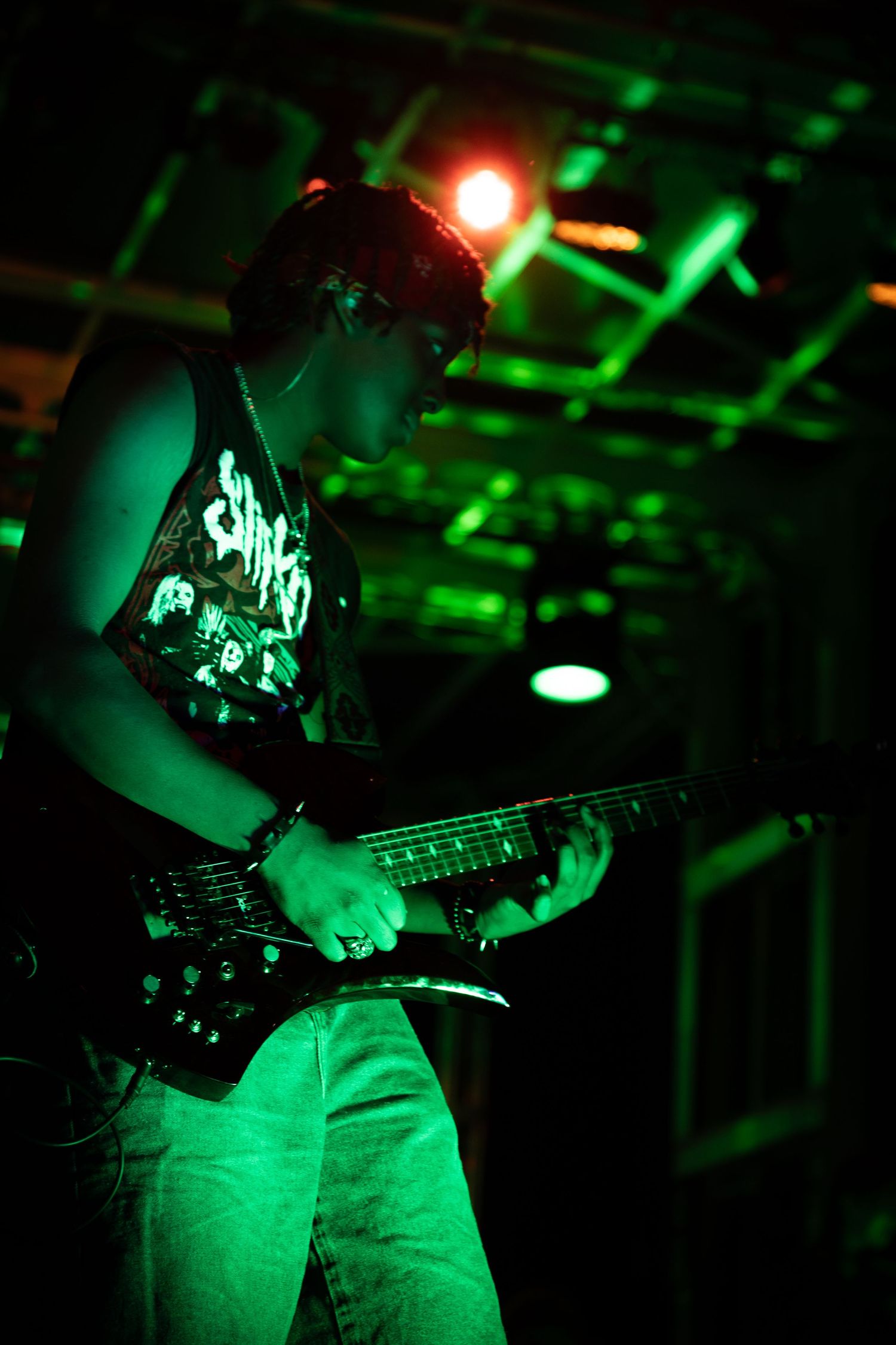 Electric guitarist playing intensely under green stage lights wearing a Slipknot tank top at a concert.