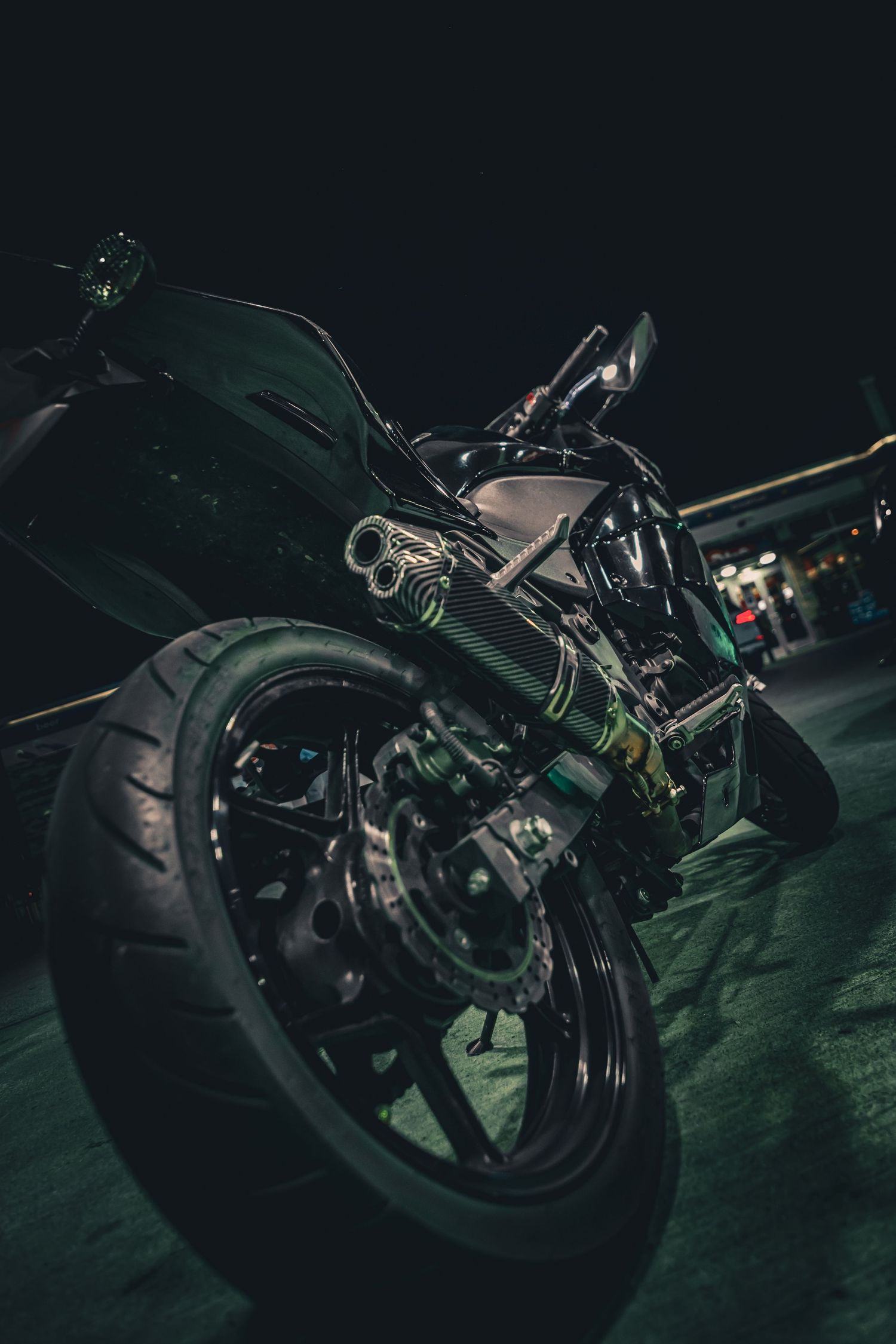 Low-angle rear view of a black sport motorcycle with green accents and exhaust pipes at night.