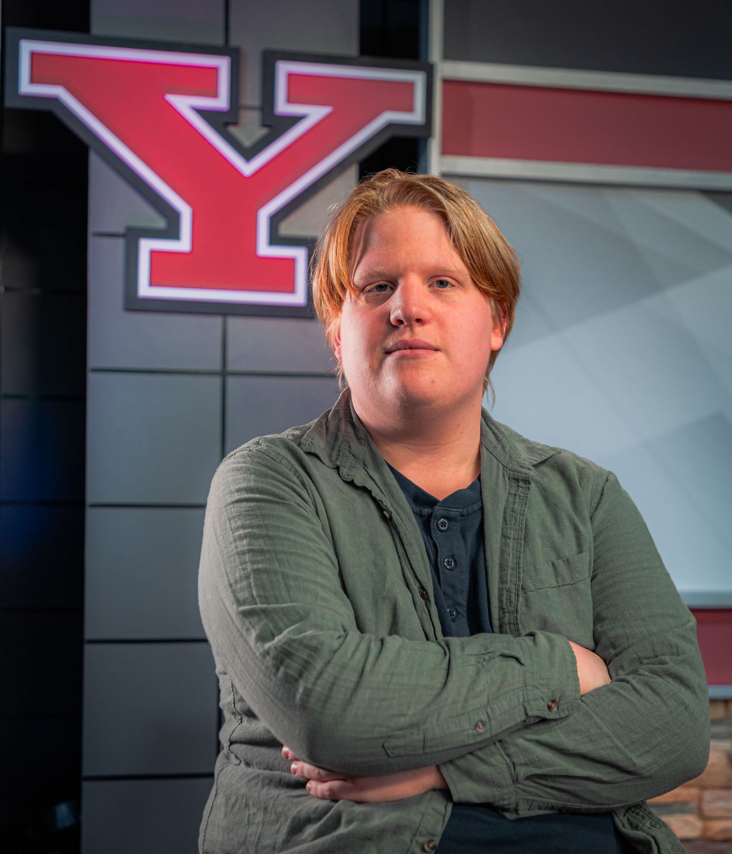 Student poses with arms crossed in front of a large red Y logo at Youngstown State University.