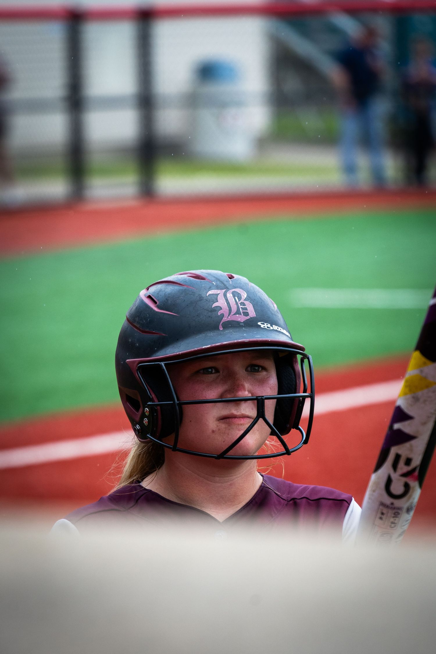 Softball player wearing maroon uniform and helmet in batting stance.