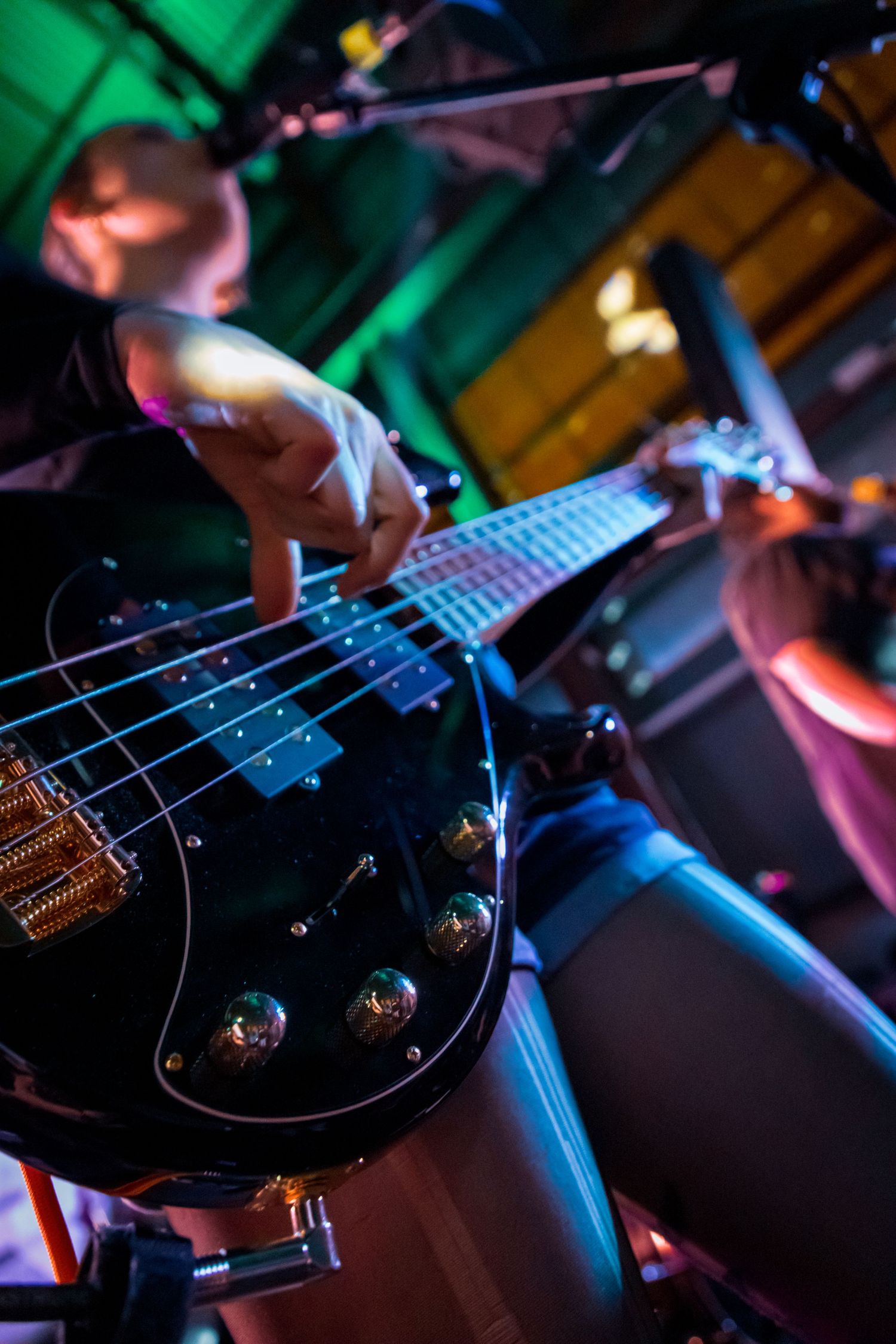 Detail shot of black bass guitar strings and fretboard under colorful stage lighting.