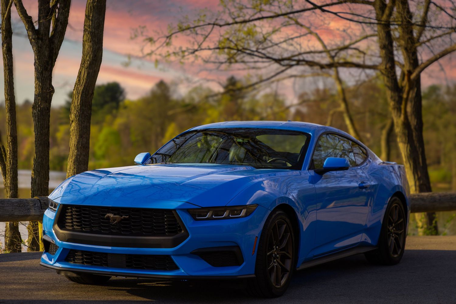 Sleek blue sports car positioned on a scenic road during sunset with trees in background.
