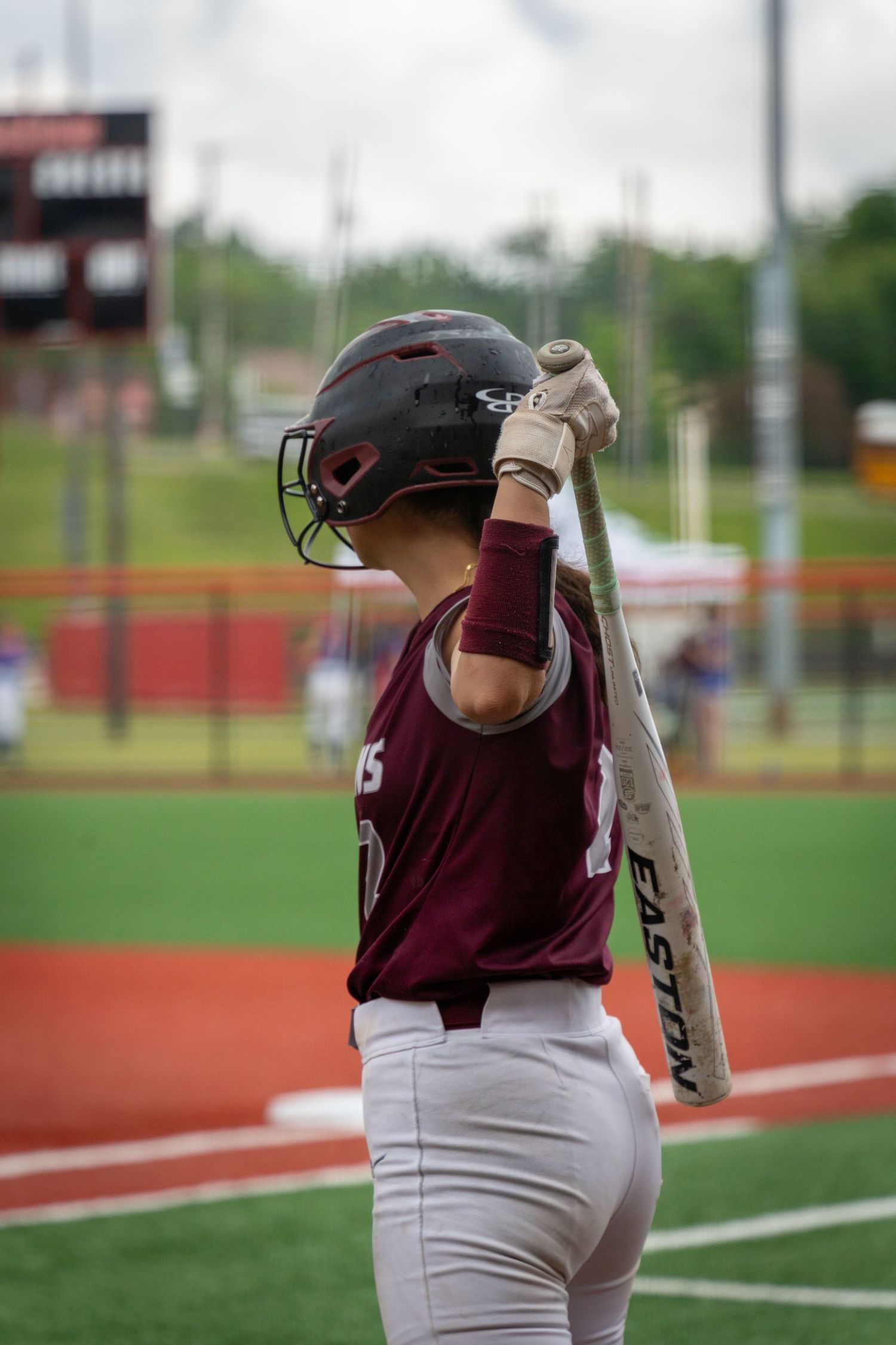 Softball player in maroon uniform swinging bat during game.