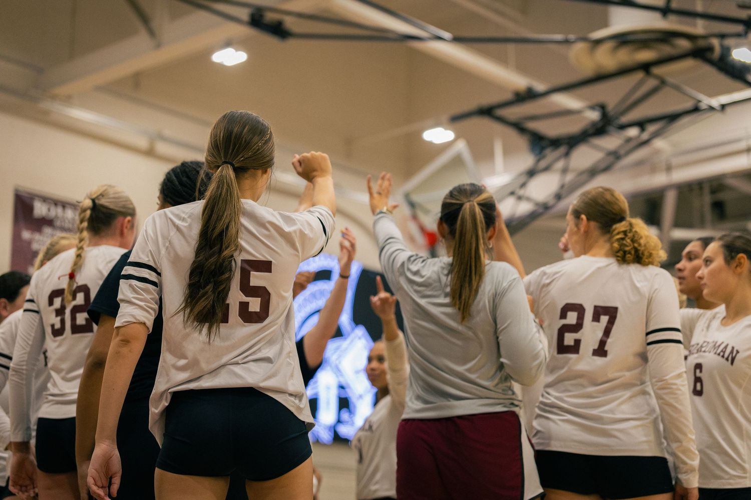 Volleyball team lineup during match with players in white and maroon uniforms.