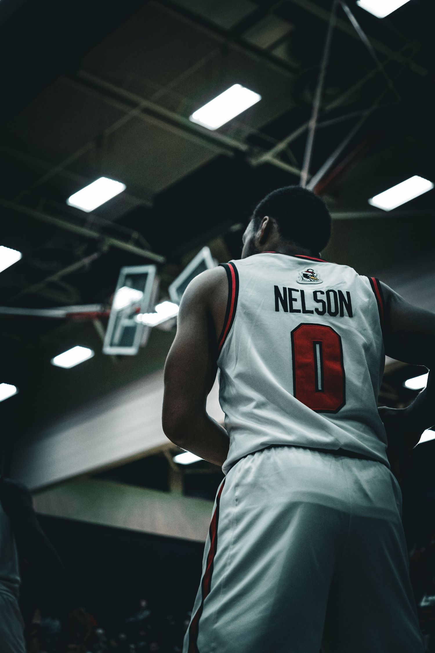 Basketball player in white jersey number 0 on dark indoor court.