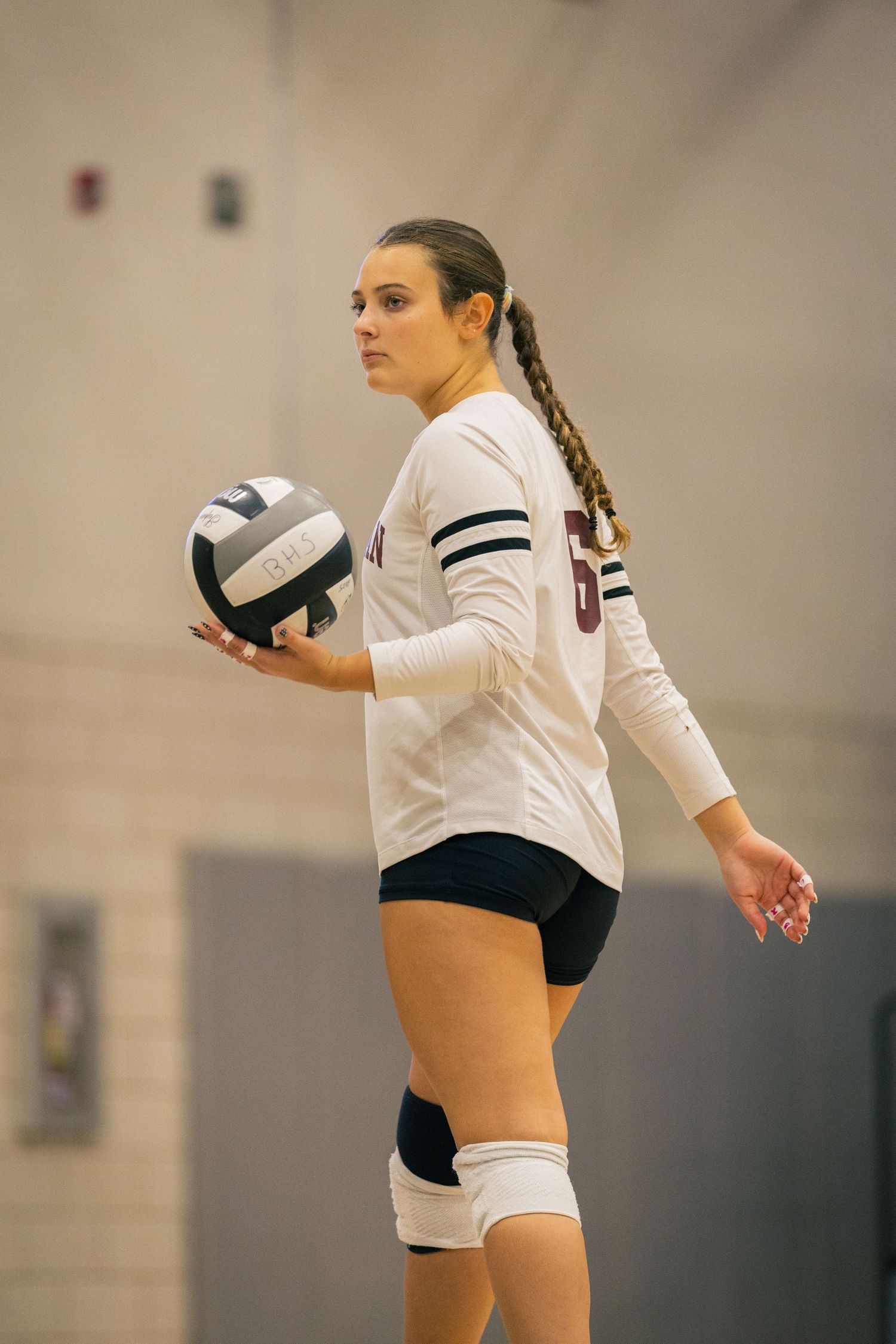 Volleyball player in white uniform preparing to serve ball during indoor match.