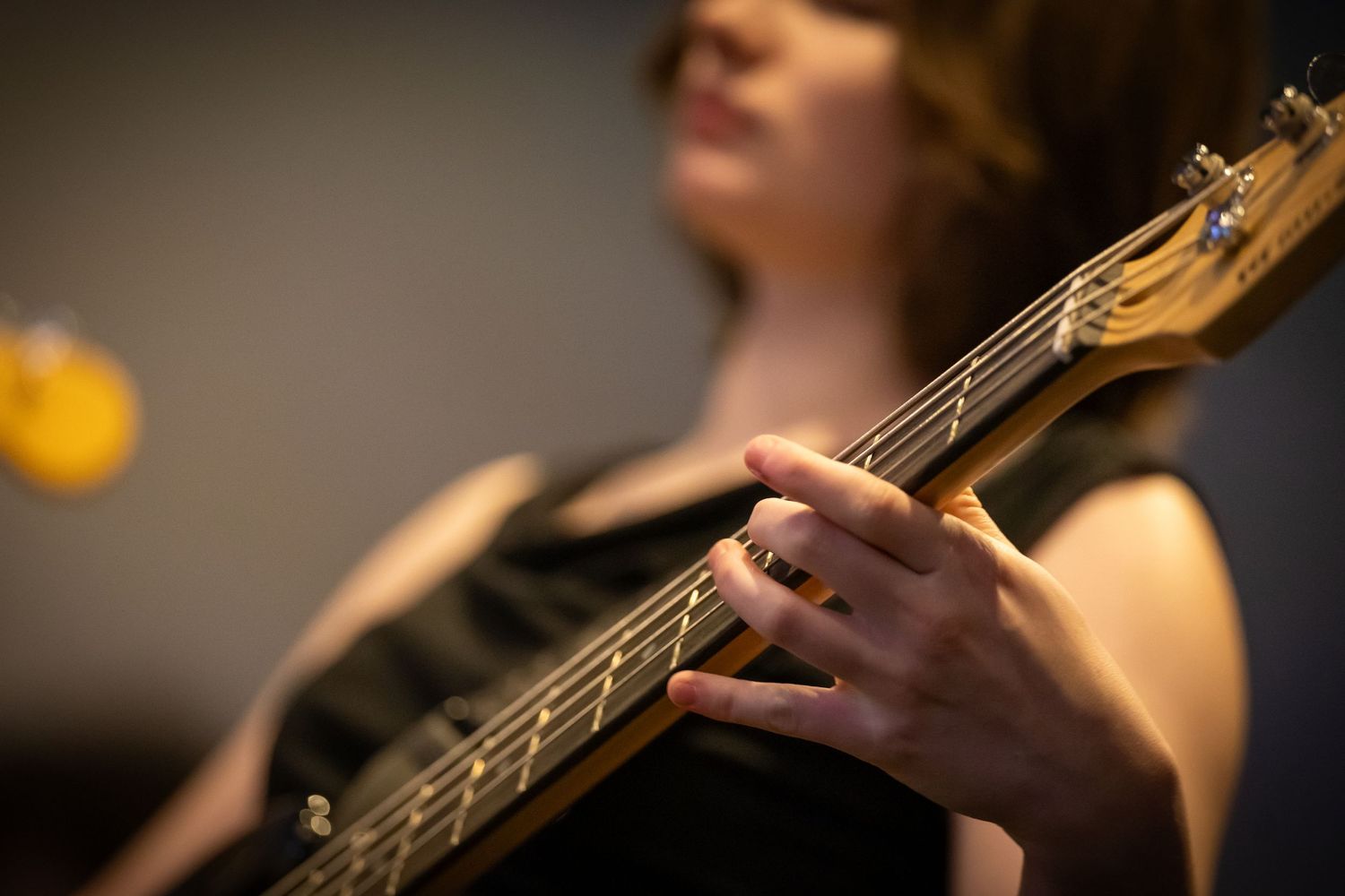 Woman in black dress playing electric guitar on stage, fingers close-up on fretboard.