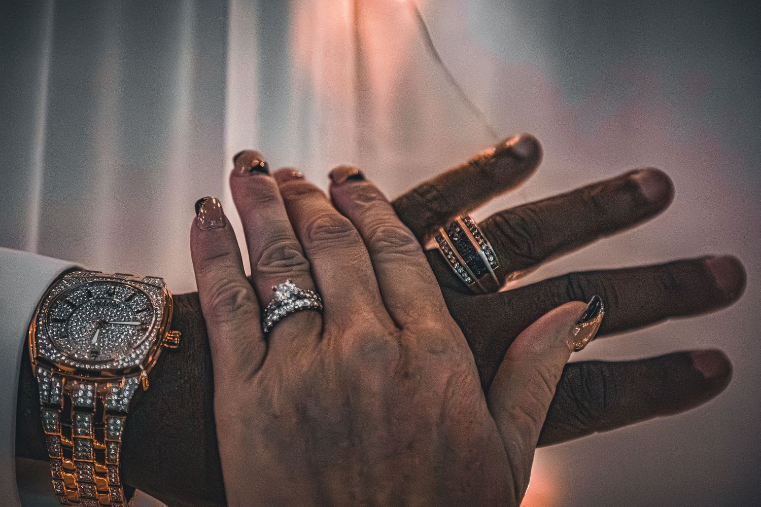 Close-up shot of hand wearing luxury watch and rings against dramatic lighting.