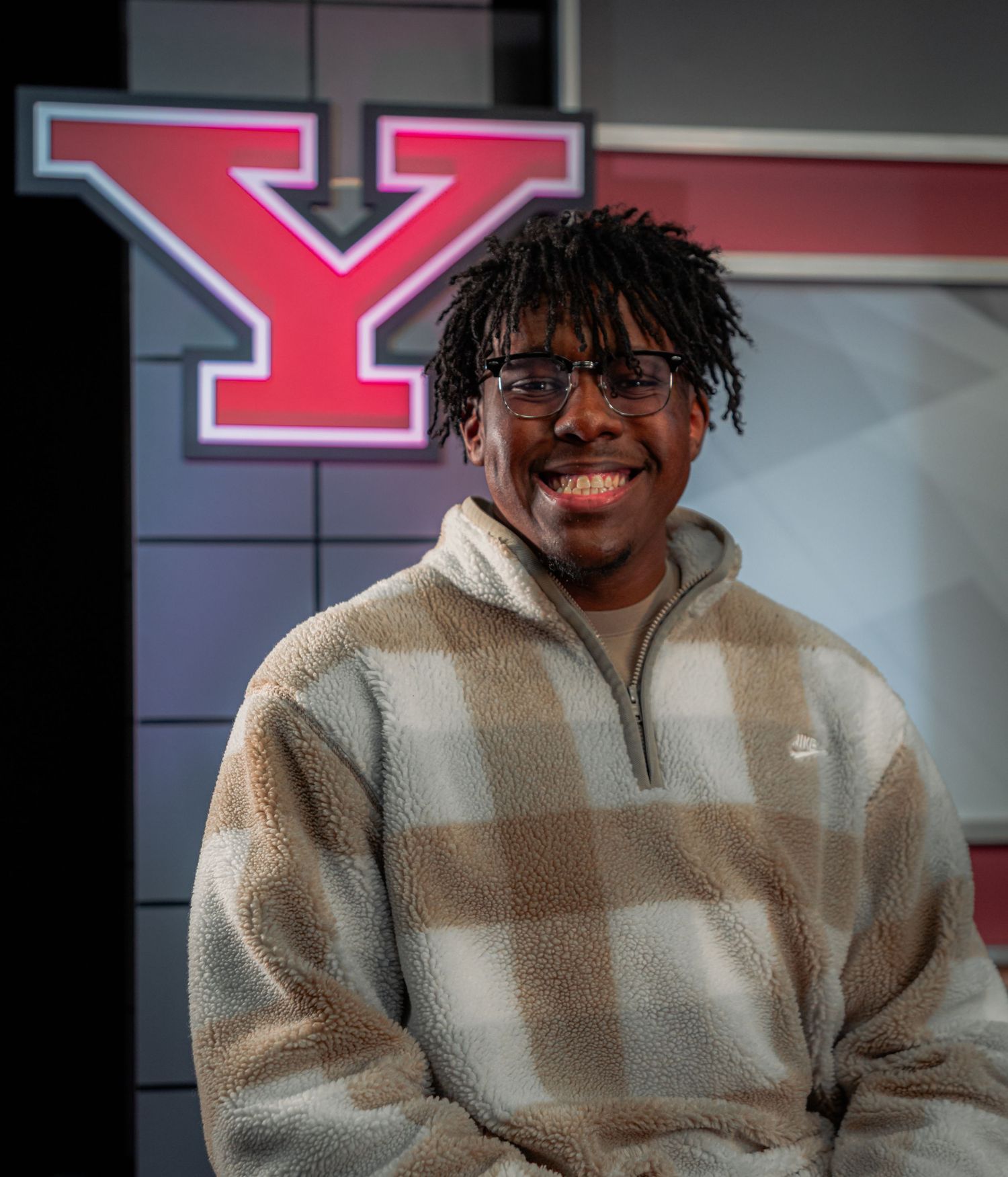 Smiling young man in a plaid fleece pullover poses in front of a red Youngstown State University Y logo.