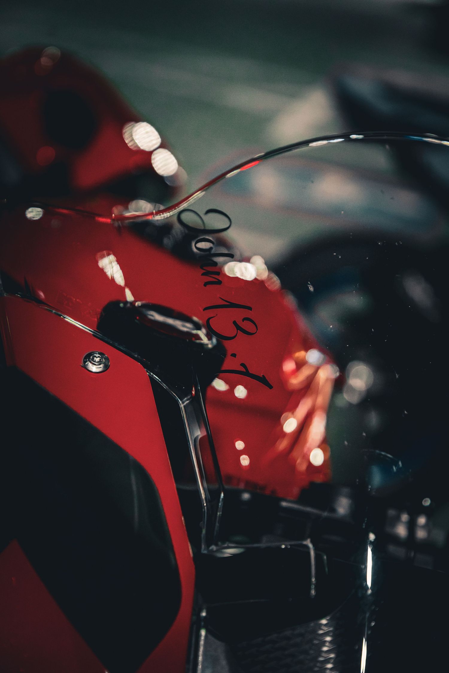Close-up of a glossy red sport motorcycle fairing with bokeh lights in the background at night.