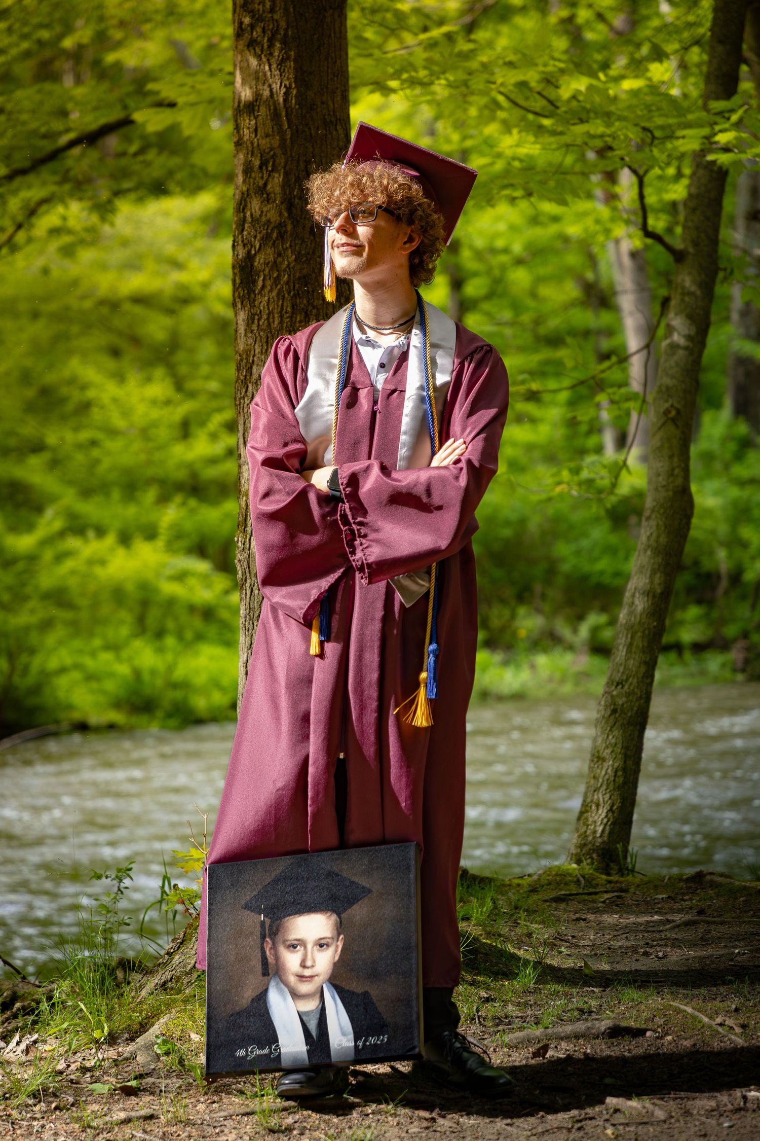 Graduation photos displayed against trees in a forest setting with burgundy gown.