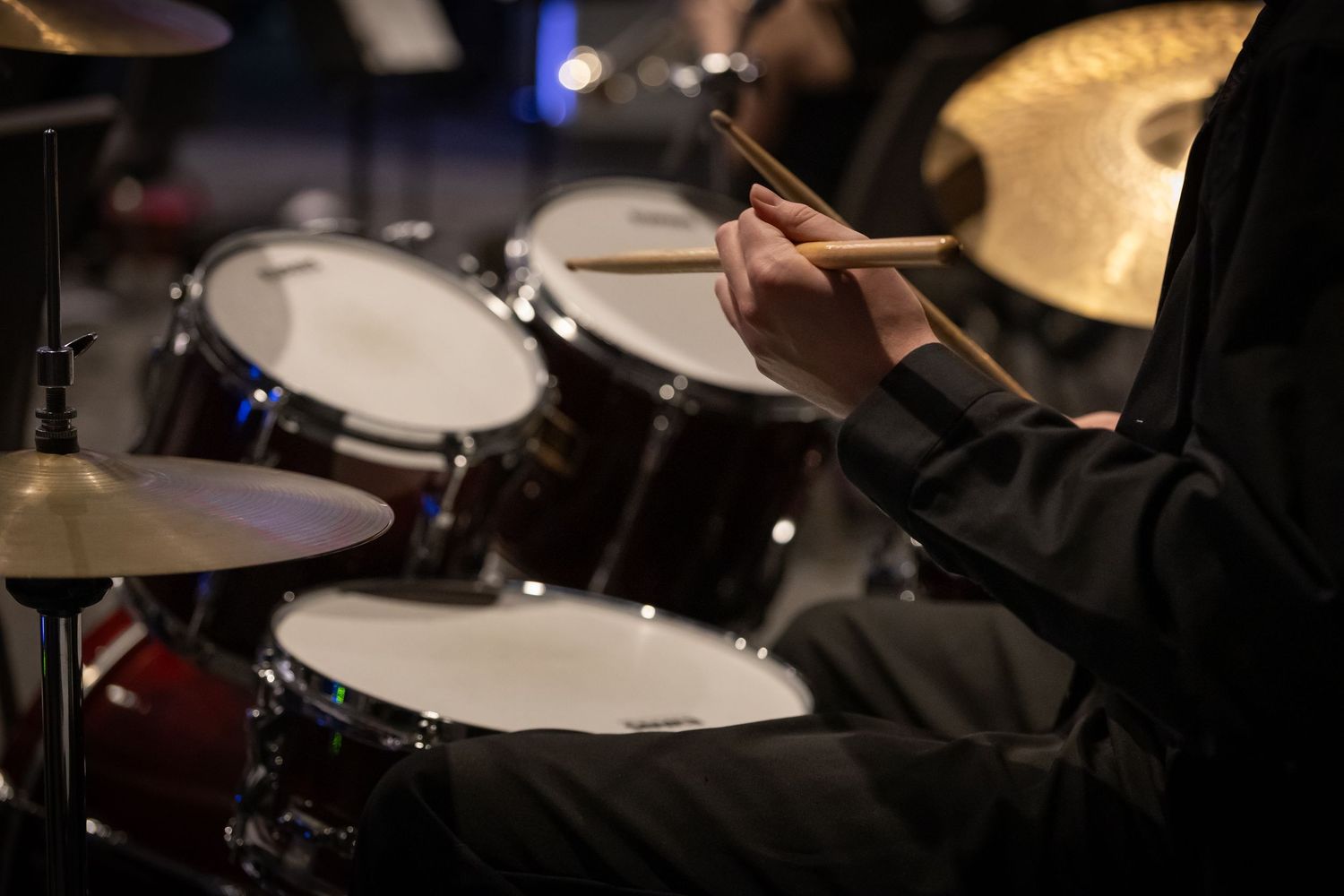 Close-up of a drummer playing a drum kit with wooden drumsticks during a live music performance.