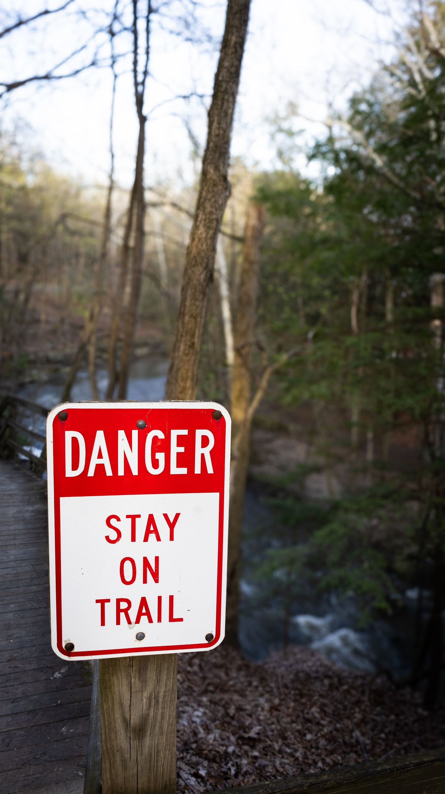 Red danger signs mounted on wooden posts warning hikers to stay on trail.