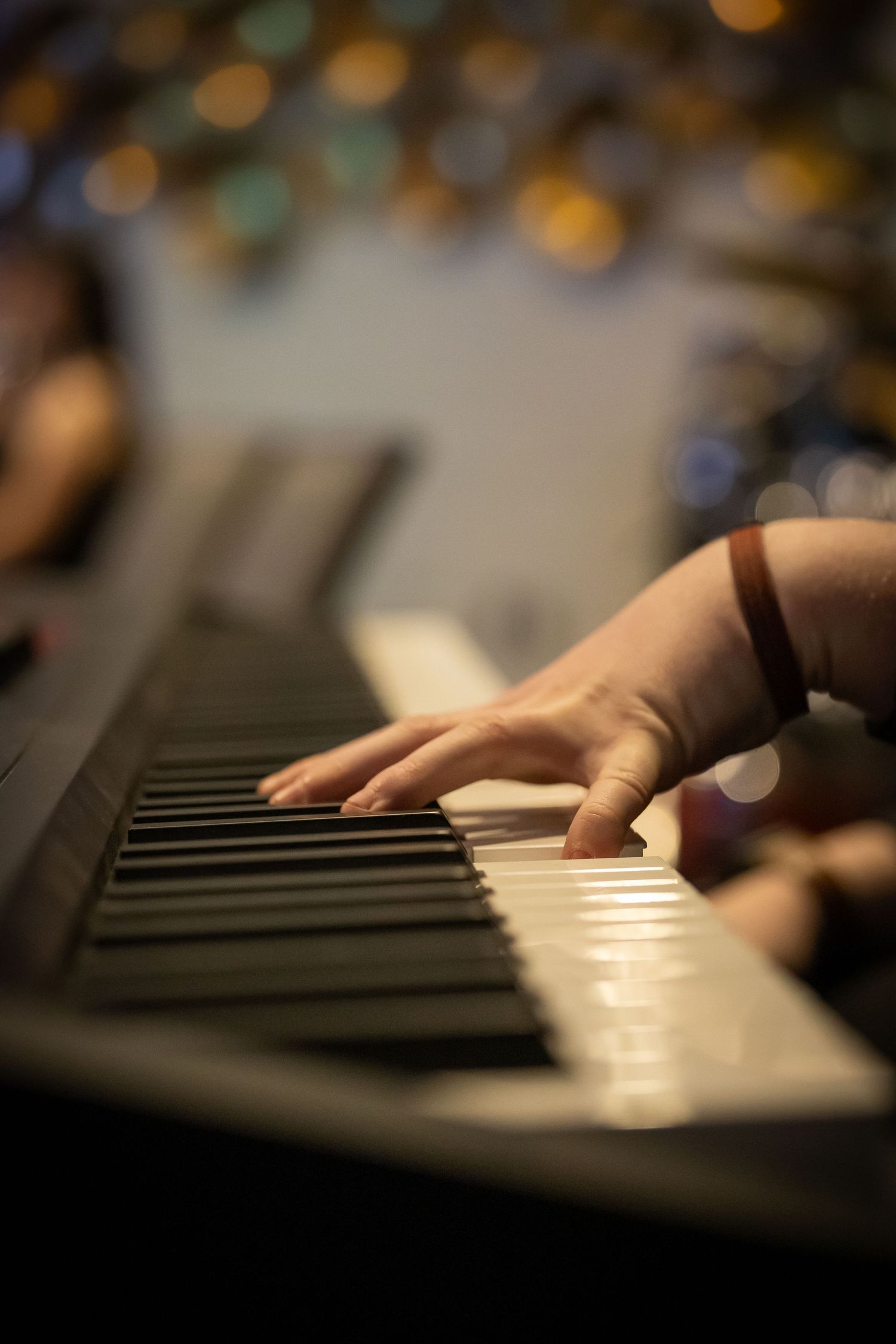 Close-up of a hand playing keys on an electronic keyboard with warm bokeh lights in the background.