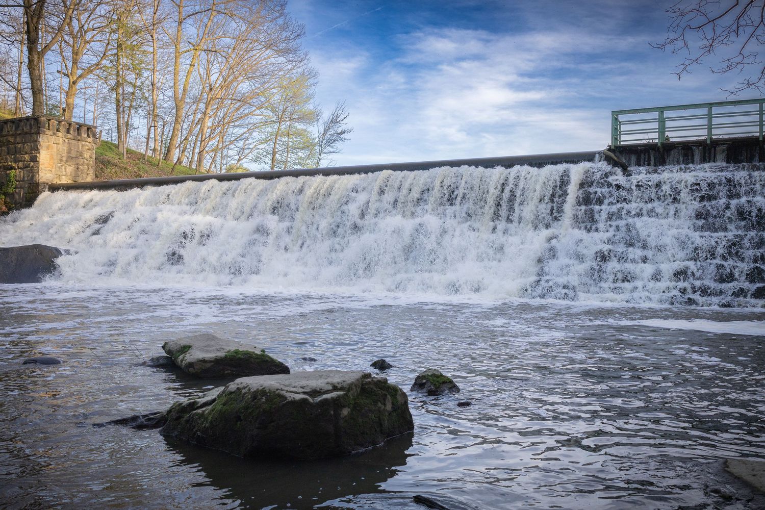 Wide waterfall cascading over a stone dam with bare trees in the background.