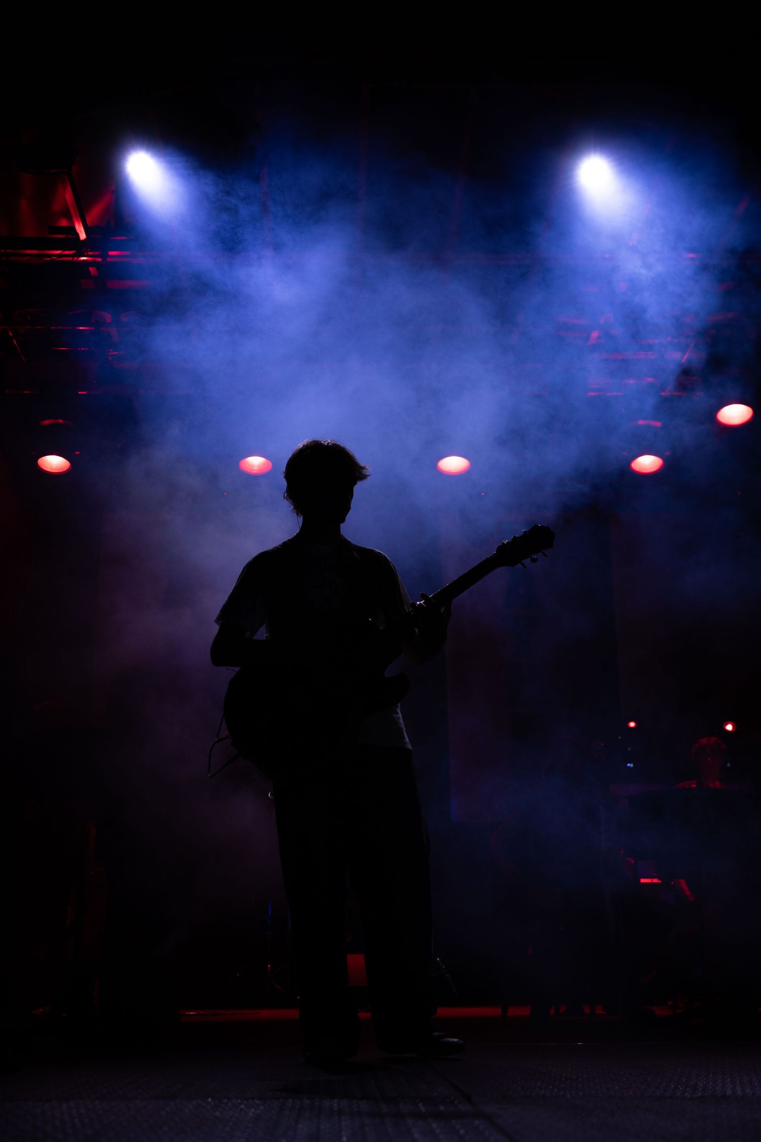 Silhouette of a guitarist performing on stage with dramatic blue smoke and colorful spotlights in the background.
