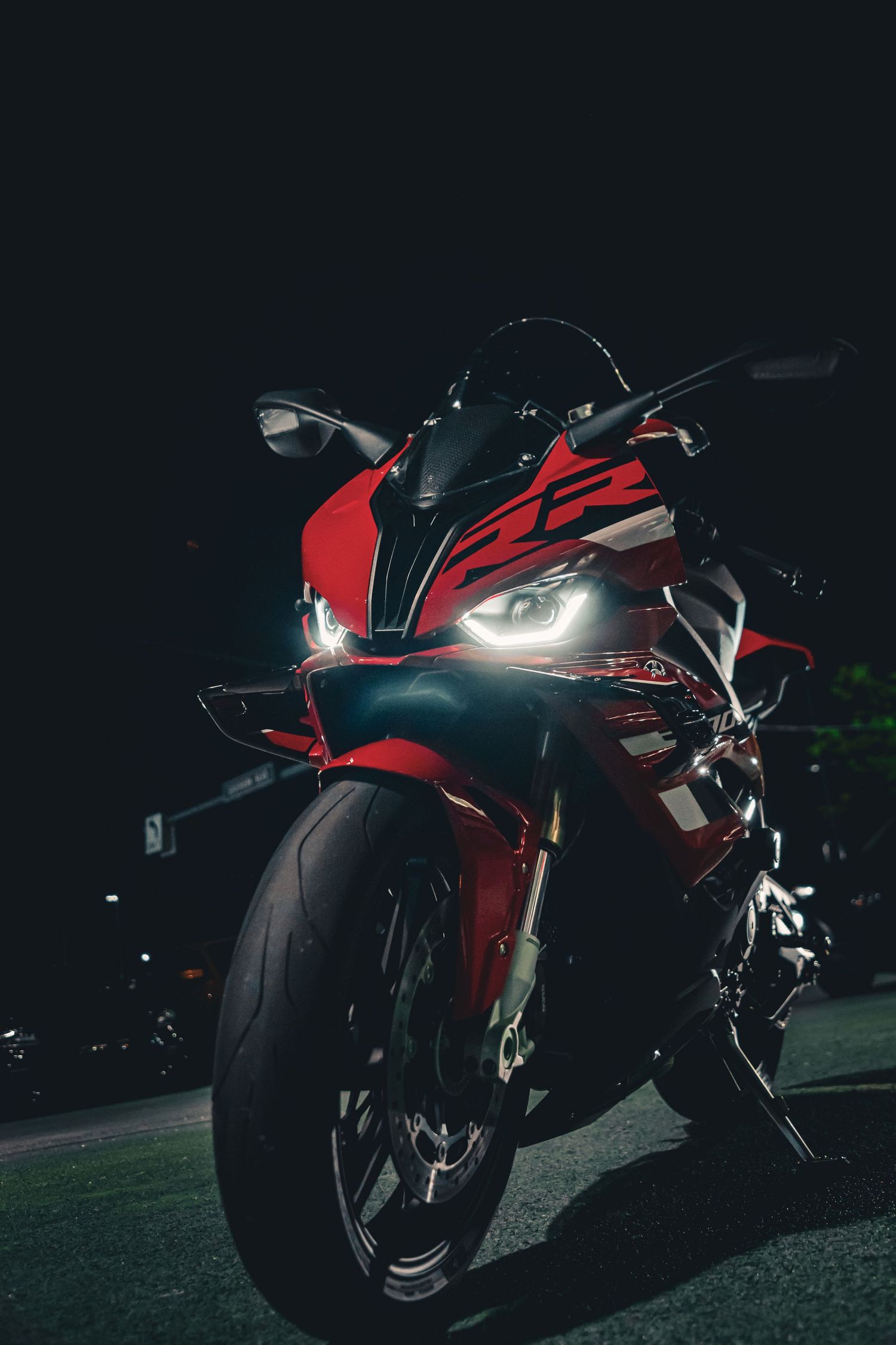 Red Ducati sport motorcycle with bright LED headlights parked on a dark road at night.