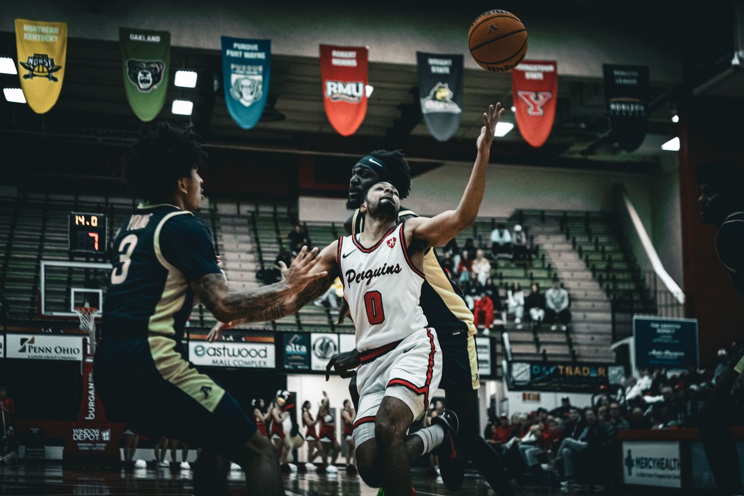 Basketball player leaps high to score during an intense game in a dimly lit gymnasium.