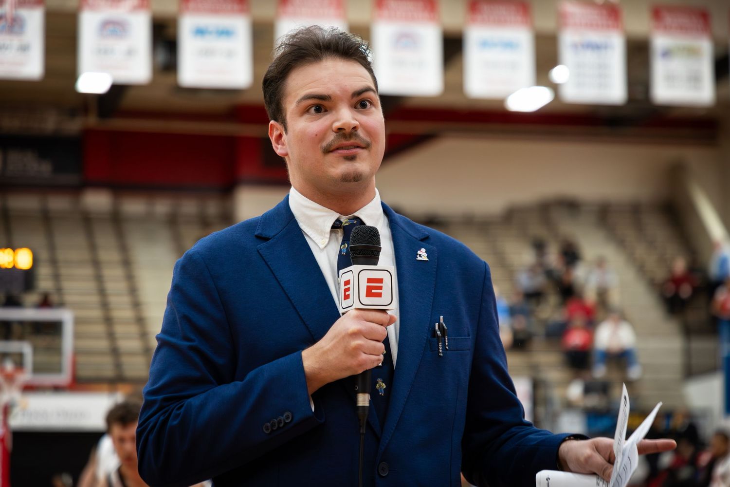 Person in blue suit speaking into microphone at indoor event.