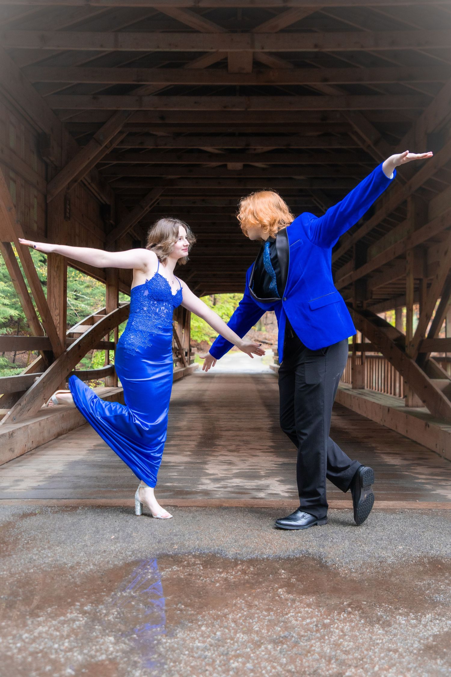 Couple in matching blue outfits dancing gracefully inside a rustic wooden covered bridge.