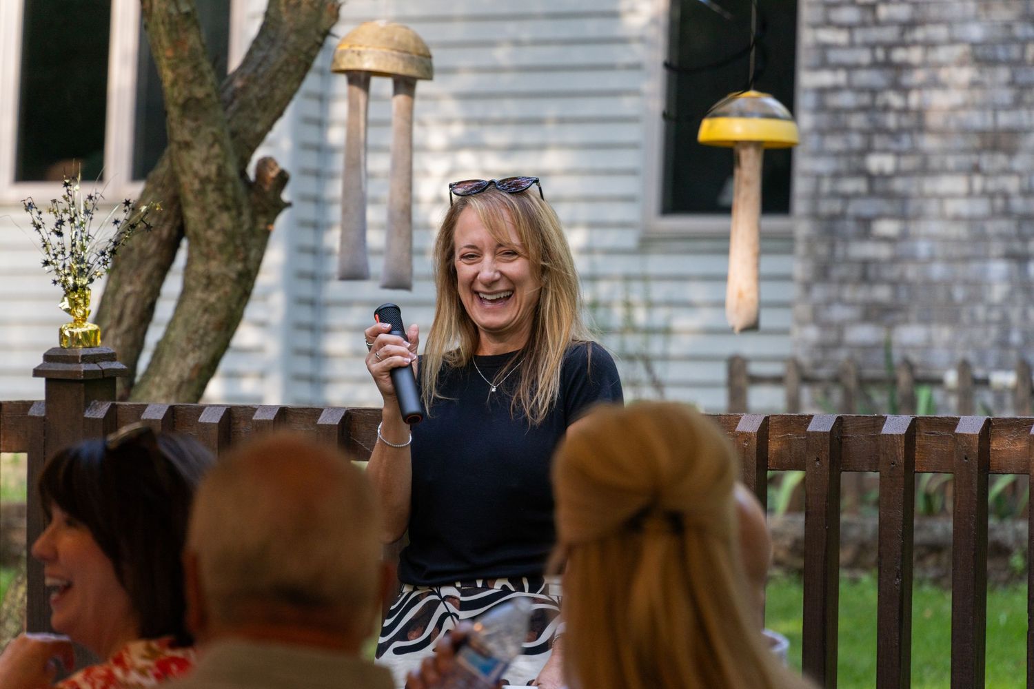 Family gathering outside a grey brick house with wooden fence in background.