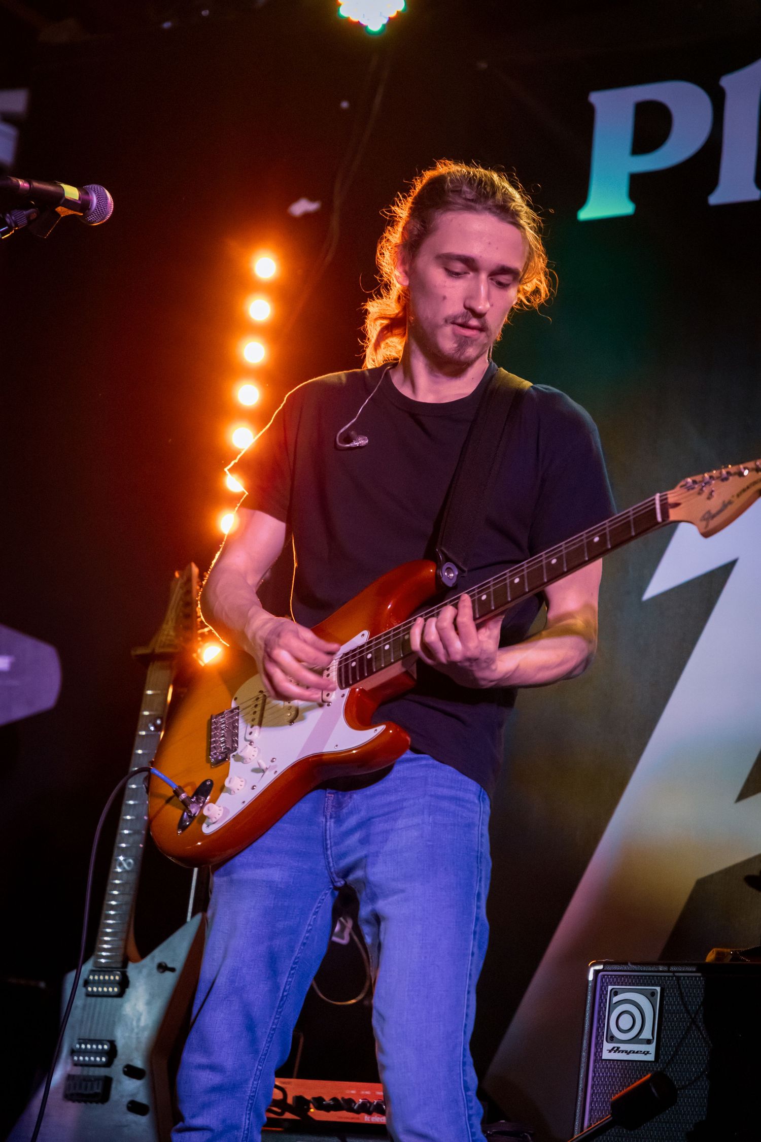 Musician playing electric guitar on stage with dramatic orange lighting effects.