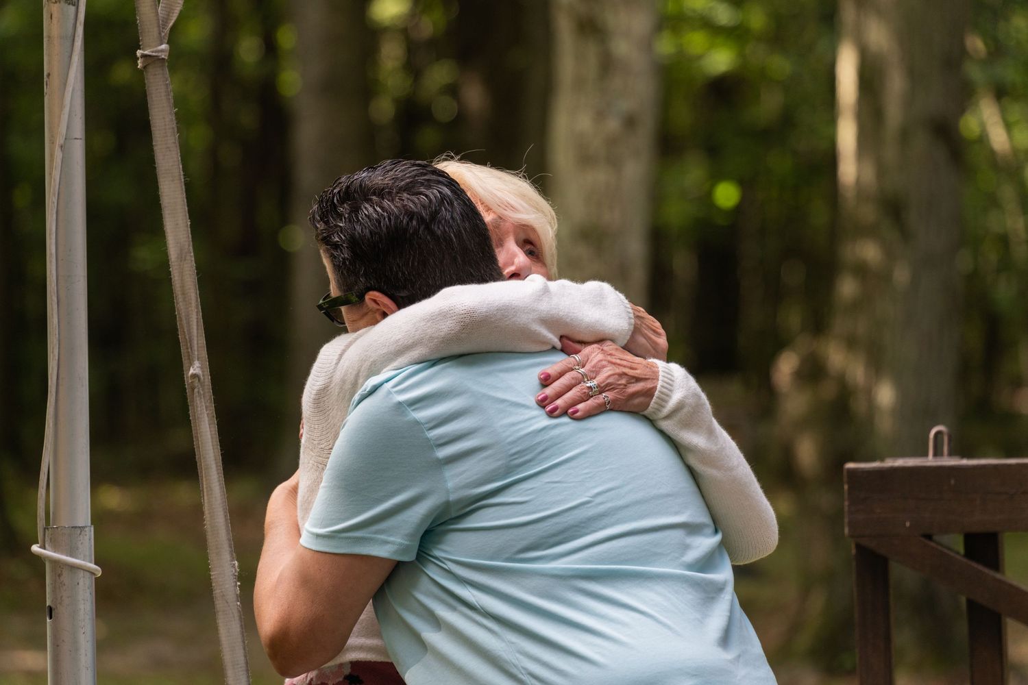 Group of people sharing warm embraces in a wooded outdoor setting.