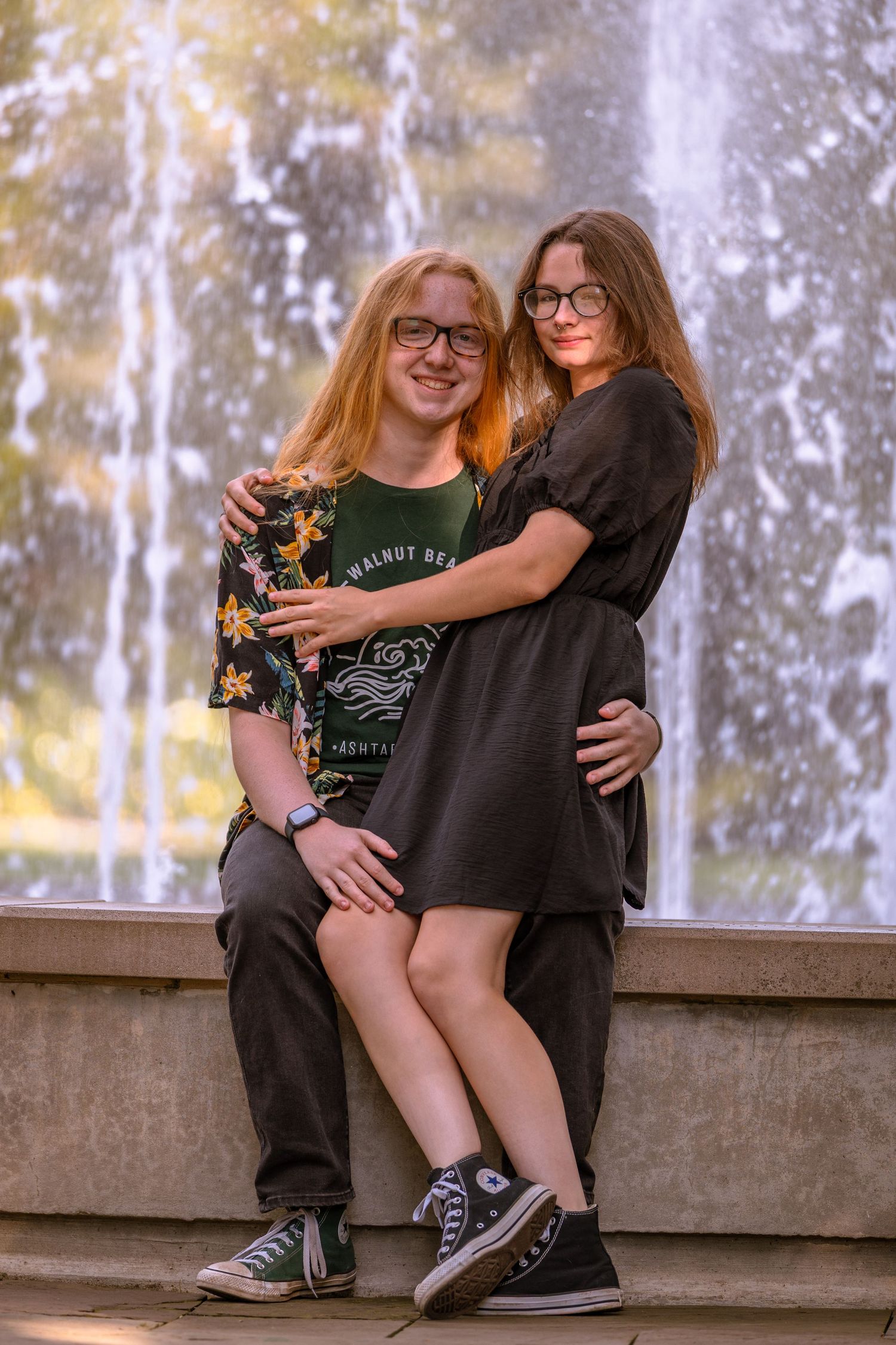 Two people sharing a casual moment together on stone steps with a fountain backdrop.