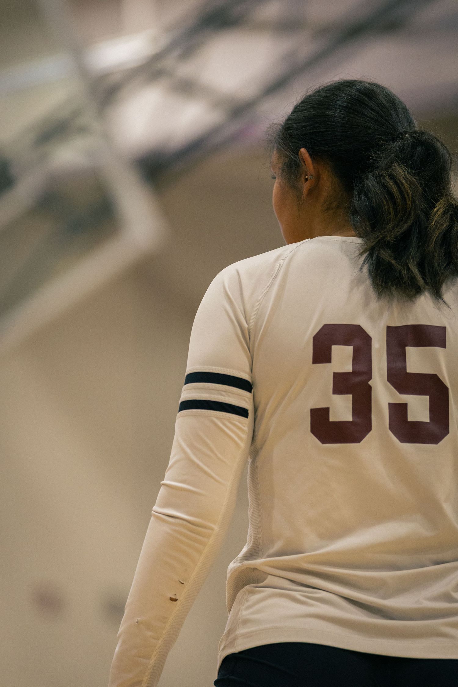 Back view of volleyball players in white jerseys with numbers during game.