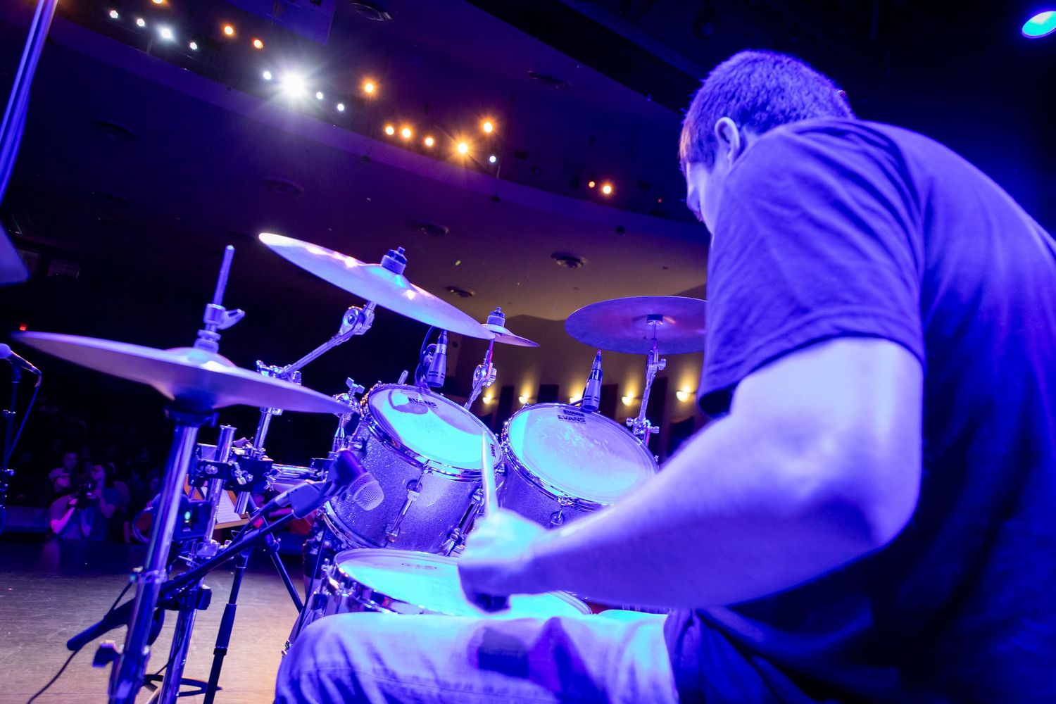 Drummer performing on stage under blue and purple stage lights during a live concert event.