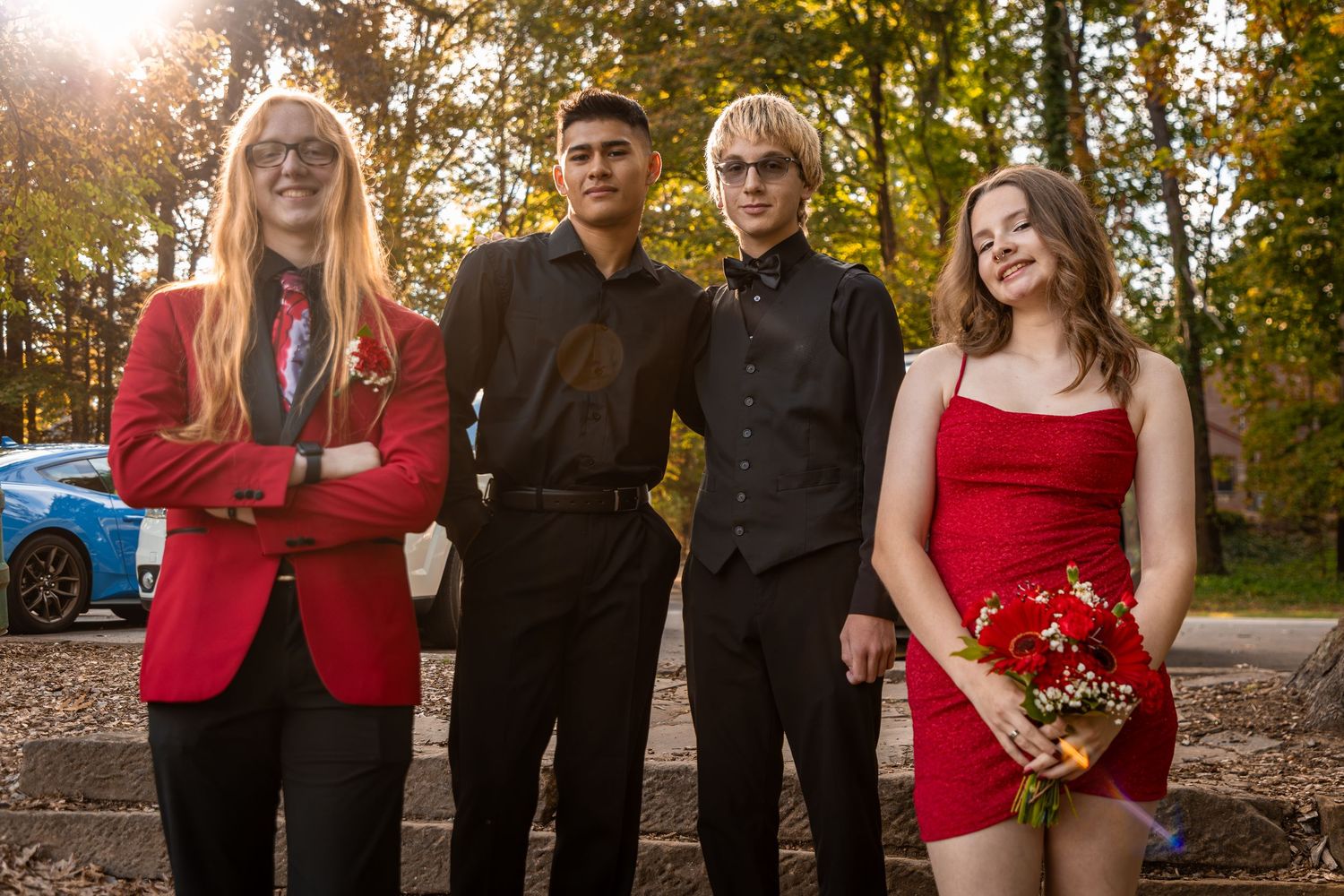 Group poses outdoors in formal attire with red and black color scheme during autumn.