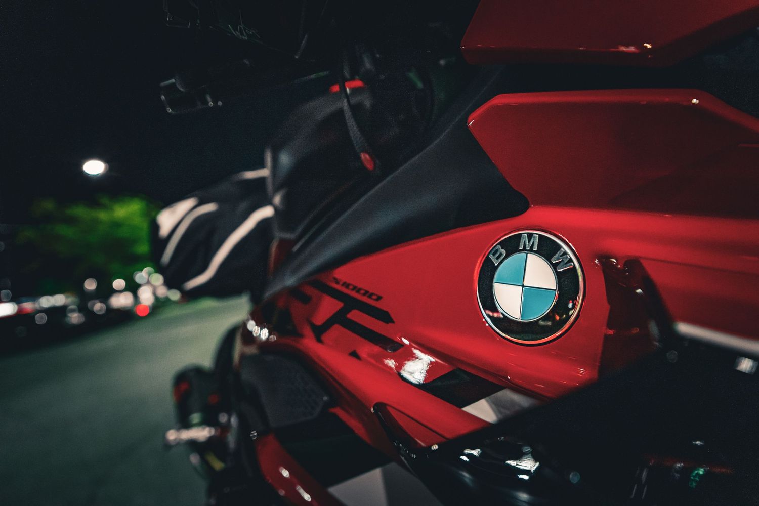 Close-up of a red BMW motorcycle with iconic BMW roundel logo, photographed at night with bokeh background lighting.