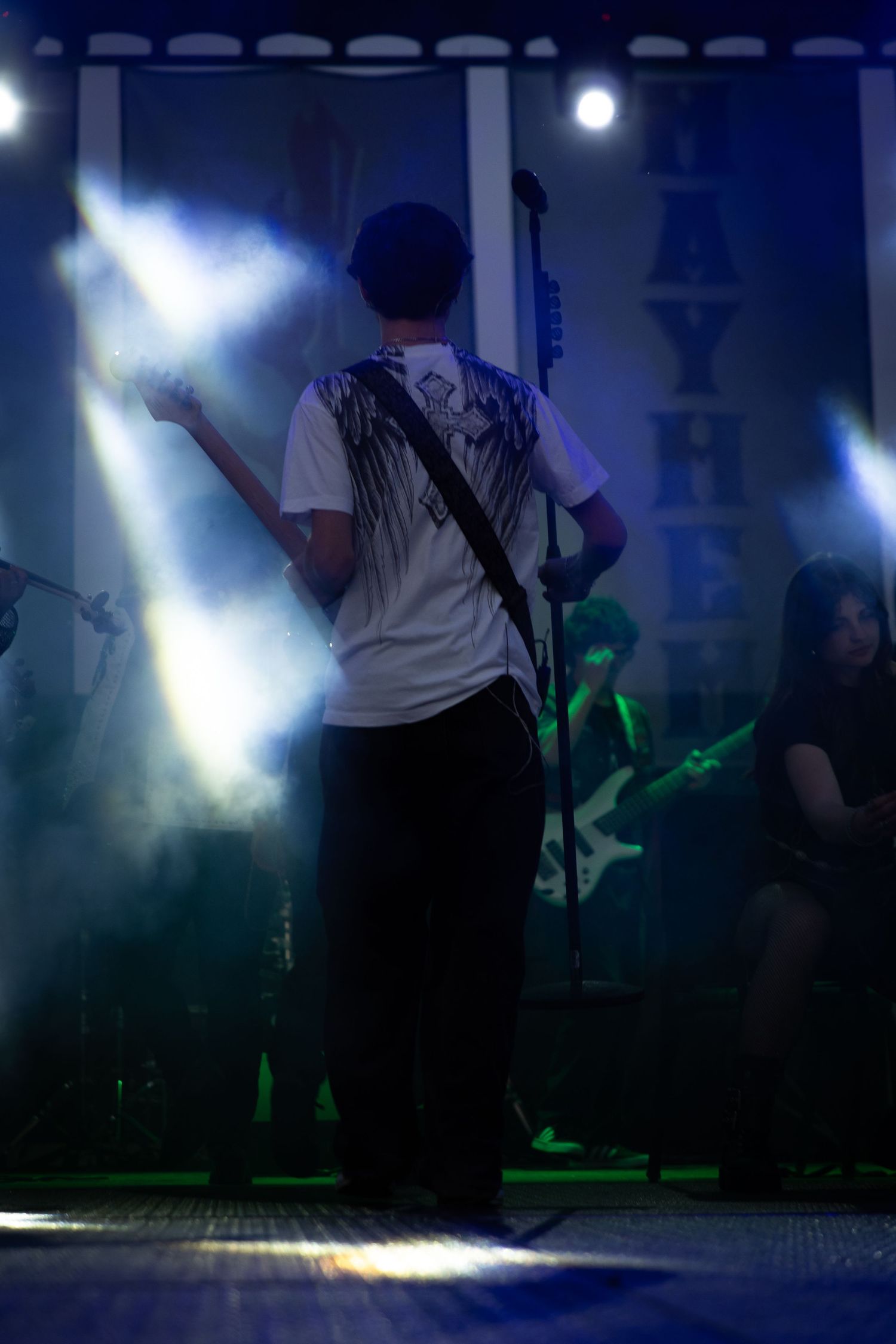 Guitarist performing on stage with dramatic blue and green lighting and smoke effects at a live concert.