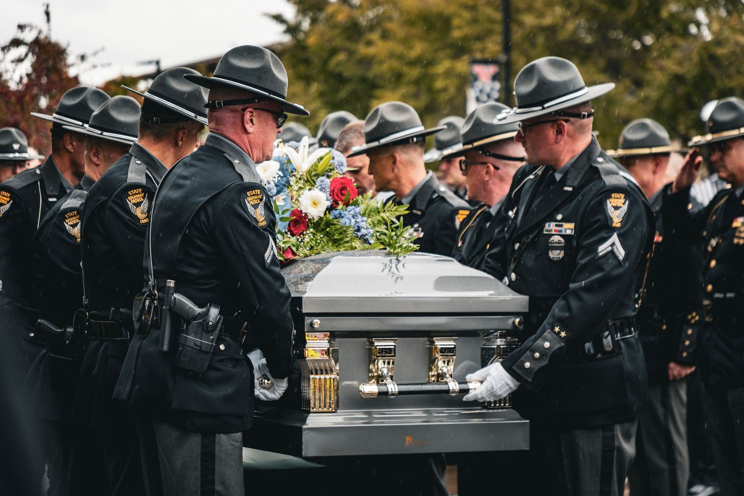 Military honor guard in dress uniforms performs ceremonial duties at outdoor service.