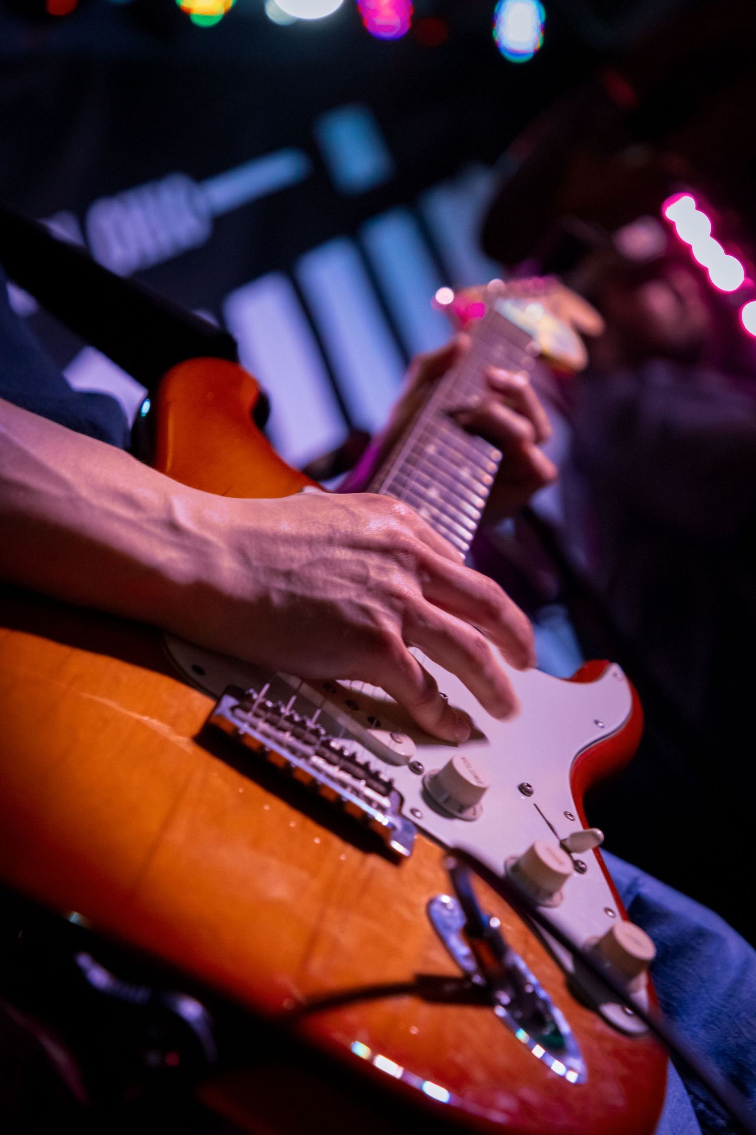 Close-up of hands playing orange electric guitar under stage lighting.