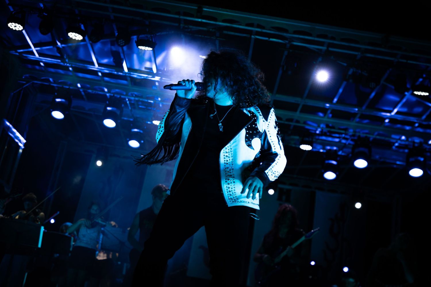A rock performer sings passionately on a dramatic blue-lit stage during a live concert performance.