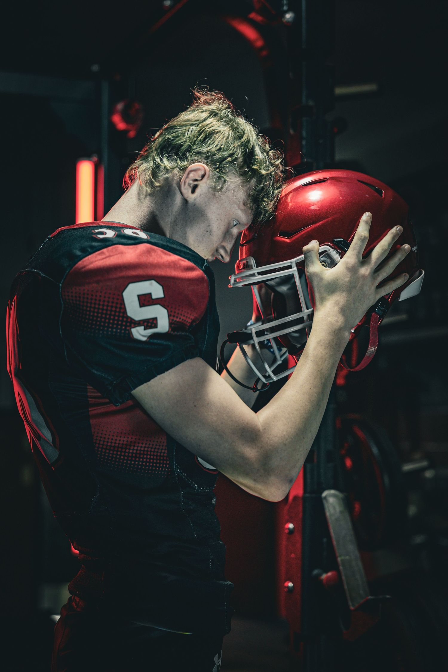 Football player in red uniform adjusting helmet in dramatic lighting.