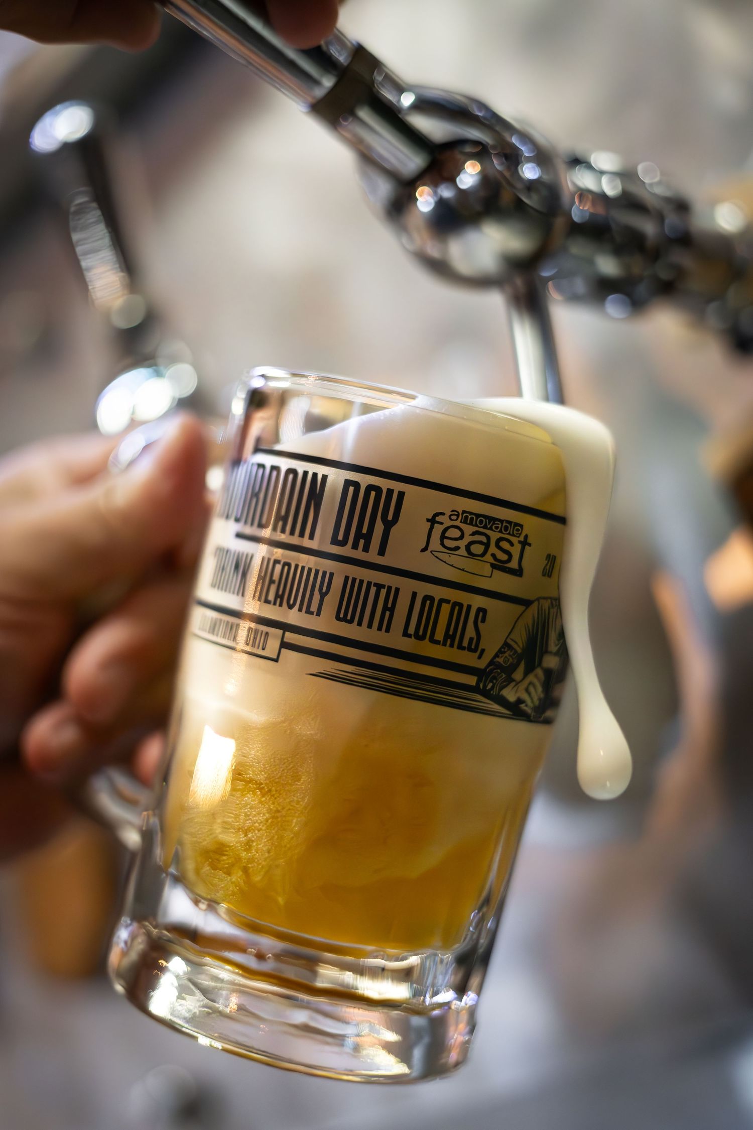 Draft beer being poured into branded glassware with foamy head.