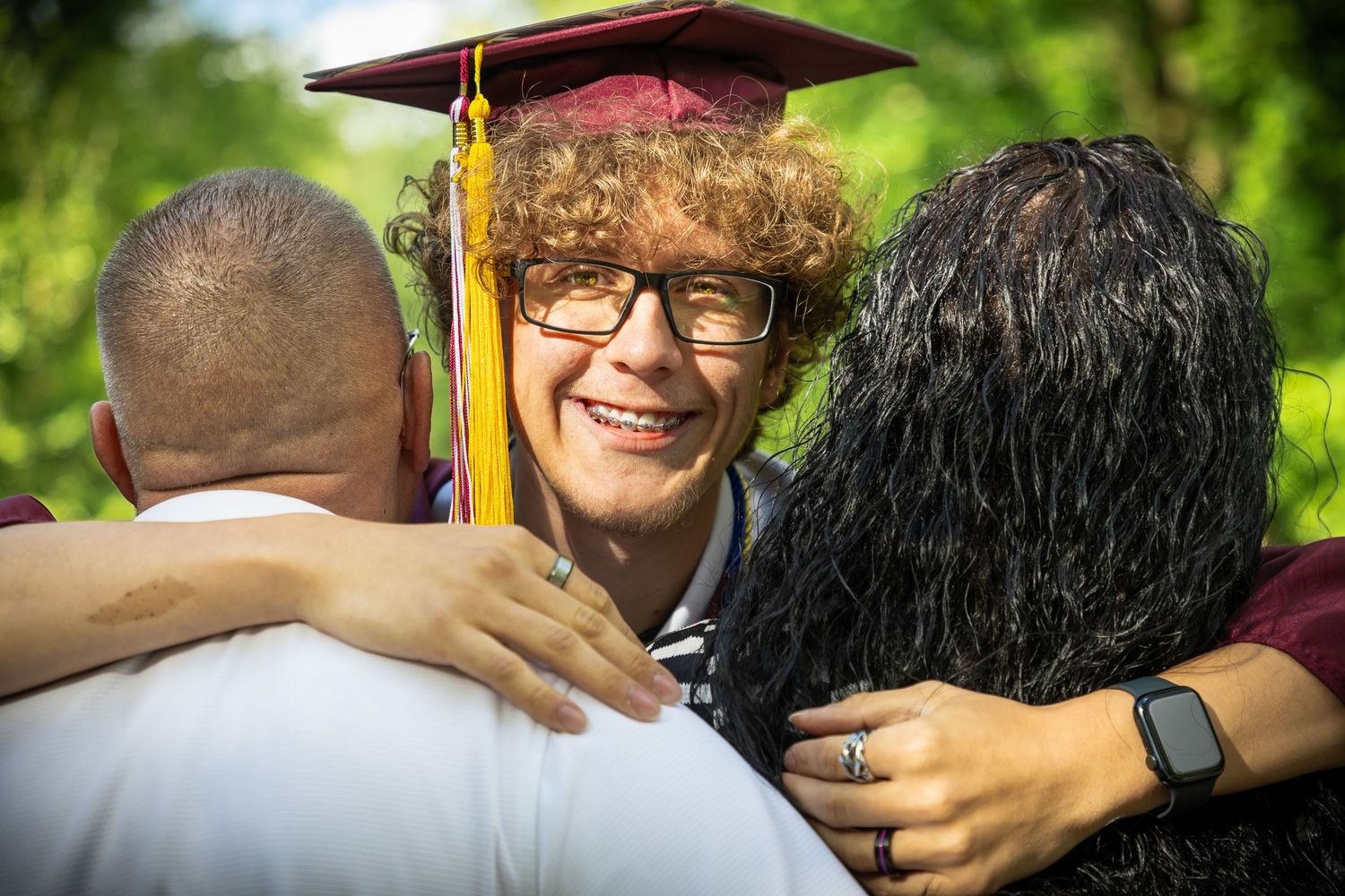 Graduates embrace in celebration wearing burgundy and white graduation attire.